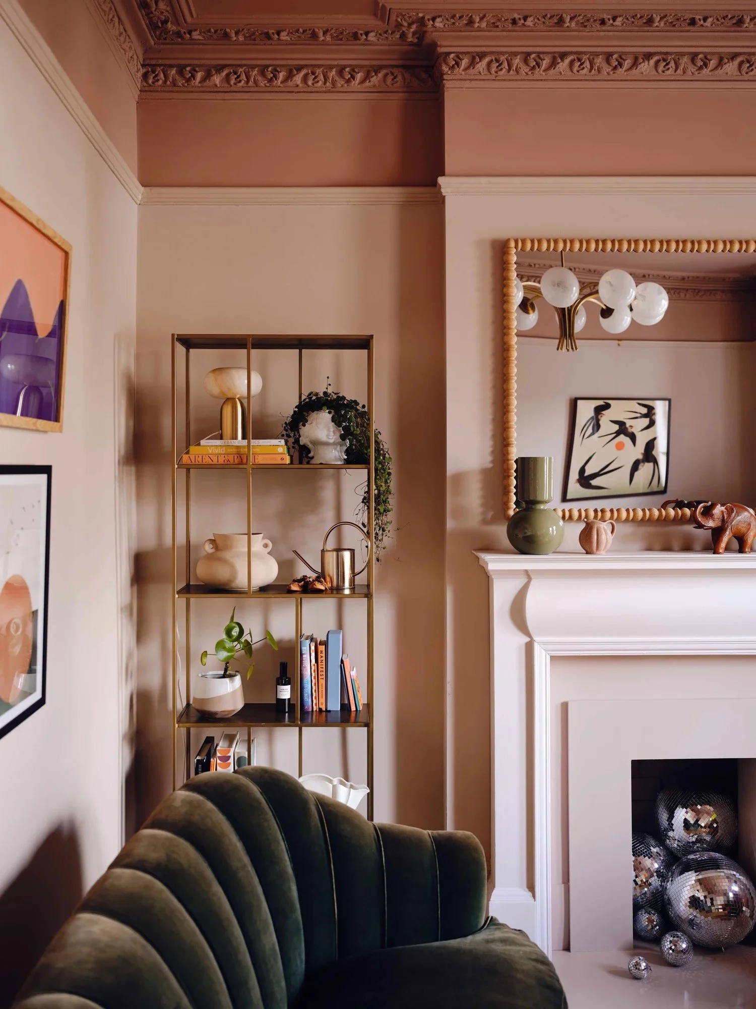 Living room corner with a mantel, decorative mirror, bookshelf, and plush green velvet chair.