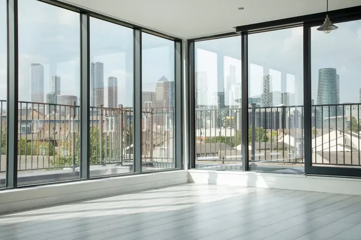 Empty modern apartment with floor-to-ceiling windows overlooking a city skyline.
