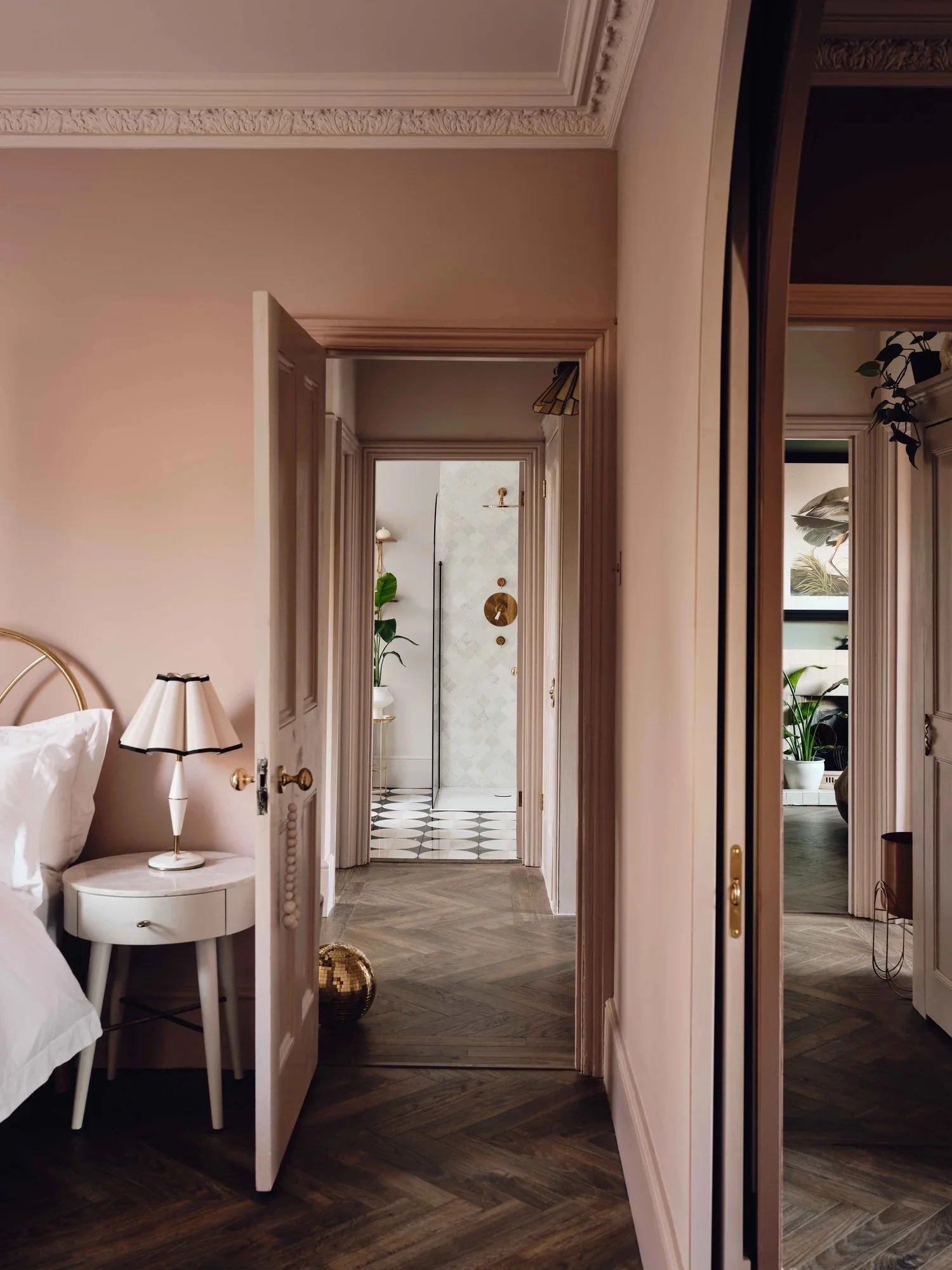 Interior view of a bedroom with an open door leading to a hallway or bathroom with patterned tiles, plants, and wall decor.