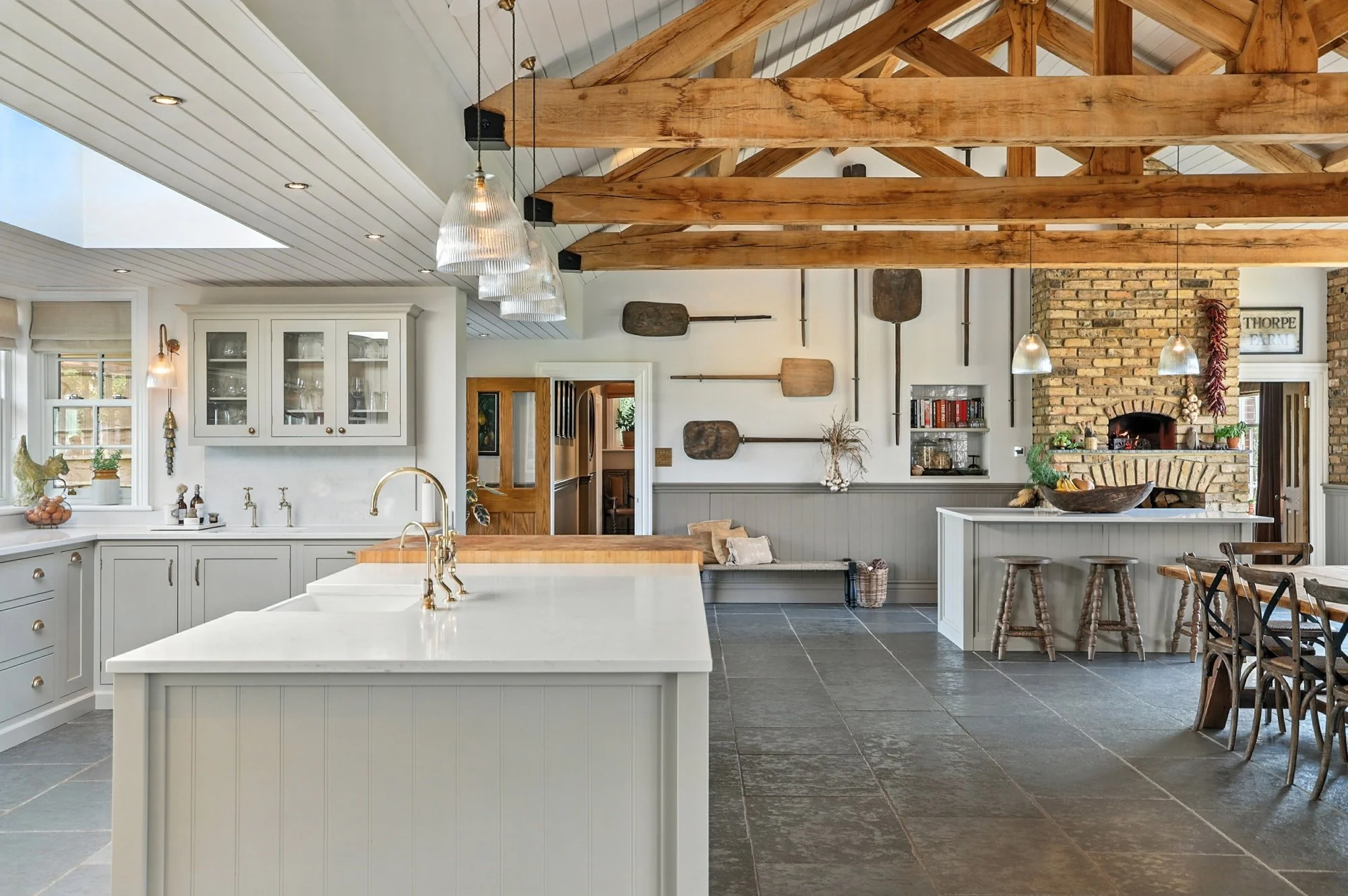 Spacious kitchen with white cabinetry, large island, exposed wooden beams, brick fireplace, and farmhouse decor.