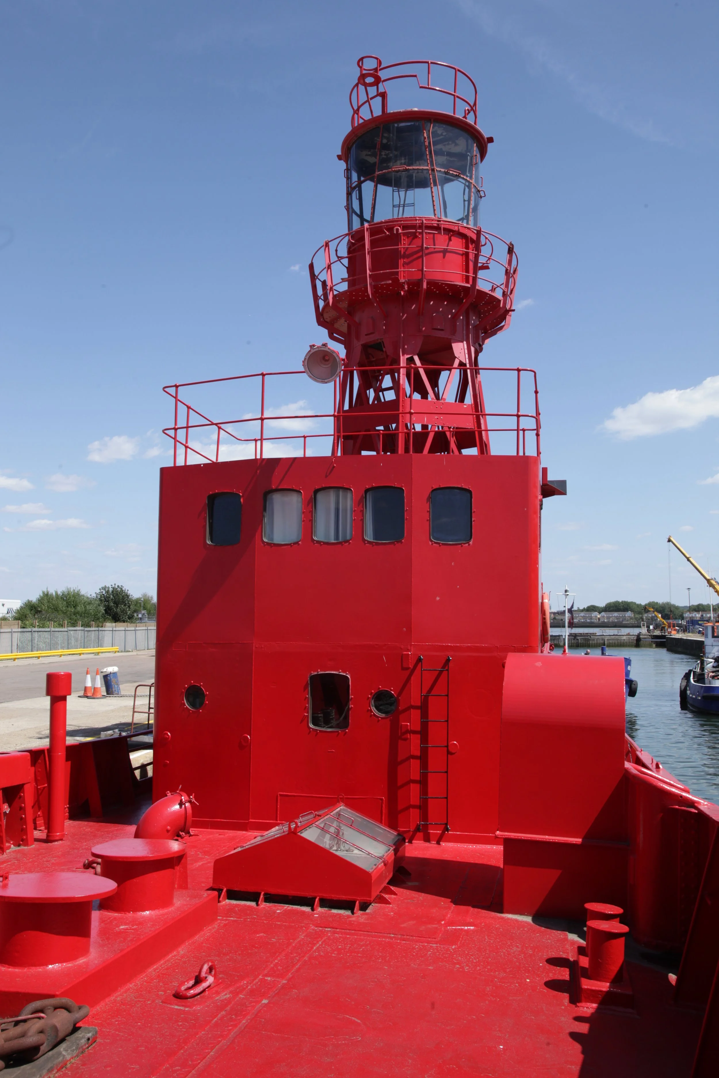 A red lighthouse on a boat docked by a marina with blue sky and a few clouds.