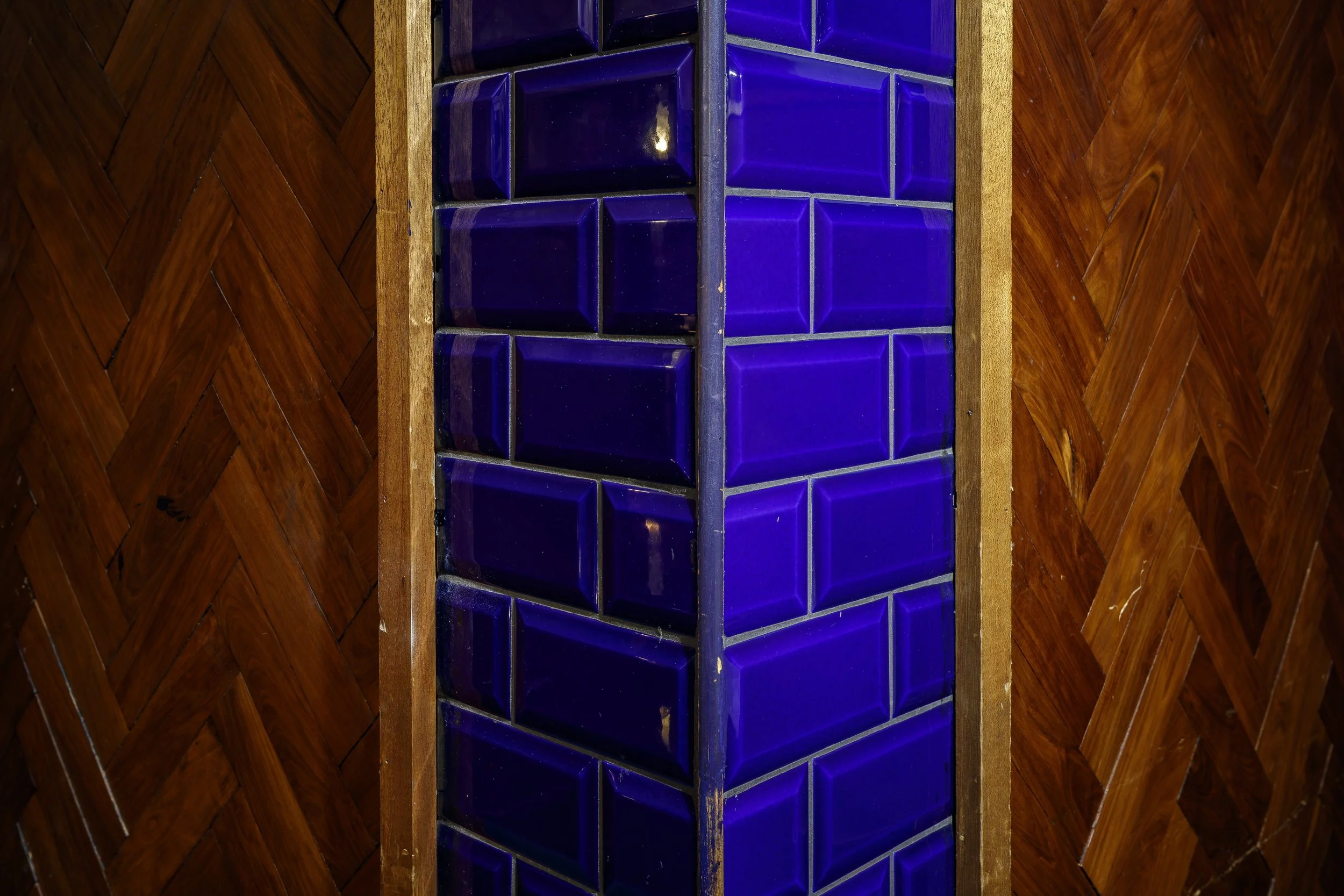 A corner with dark purple square tiles in the middle, bordered by wooden panels arranged in a herringbone pattern.