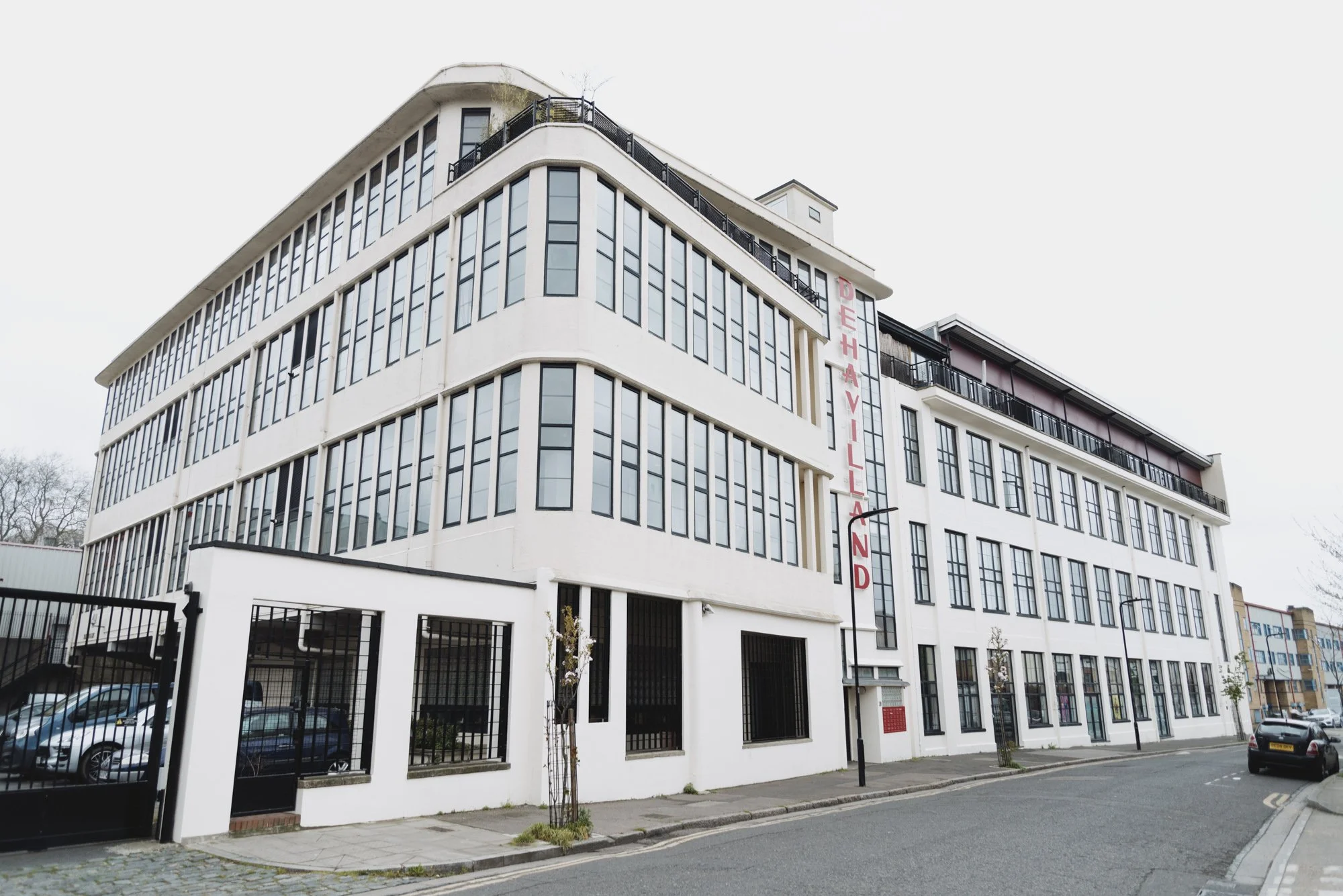 A multi-story modern building named 'DeHavilland' with large windows and a black gated parking area in the front, located on a city street.