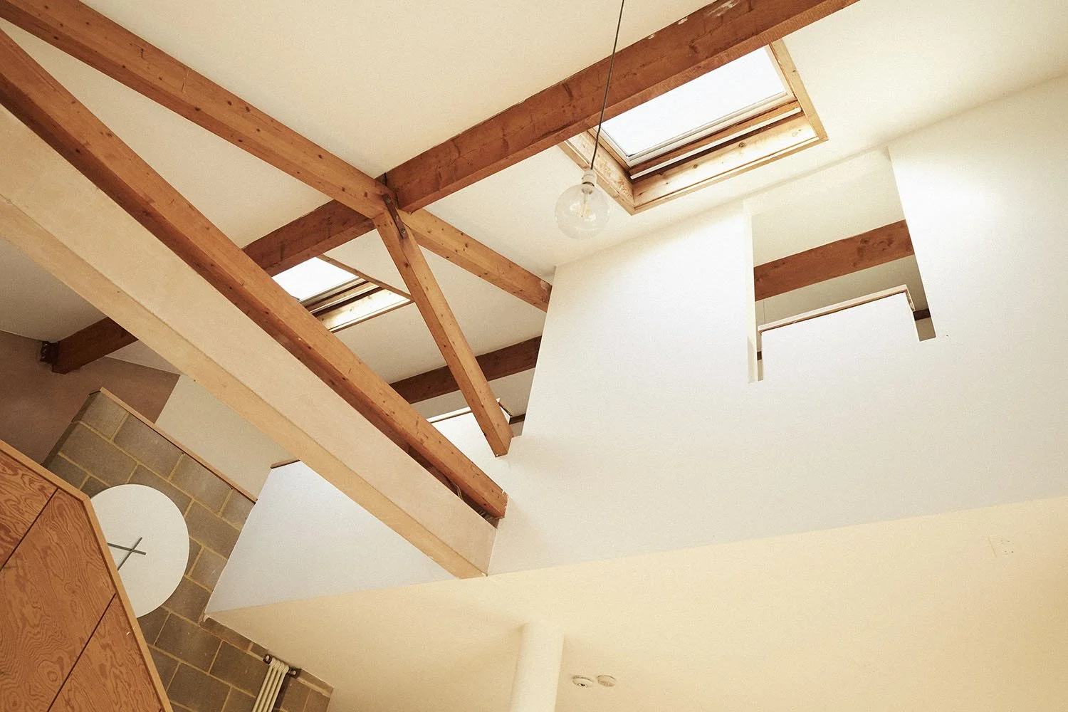 Interior view of a modern home with wooden beams on the ceiling, skylight windows, and white walls.