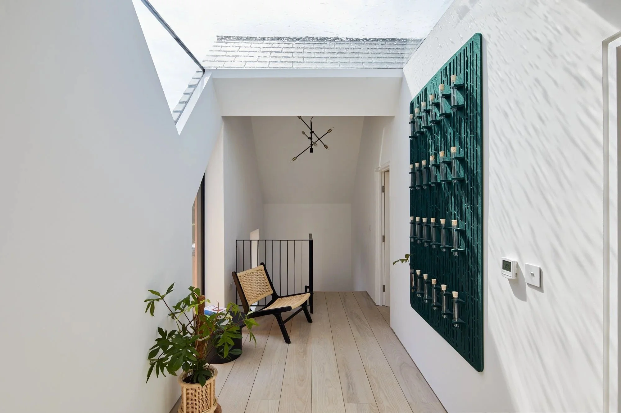 Modern interior entryway with a skylight, wall-mounted candle holder, bench, plants, and minimalist decor.