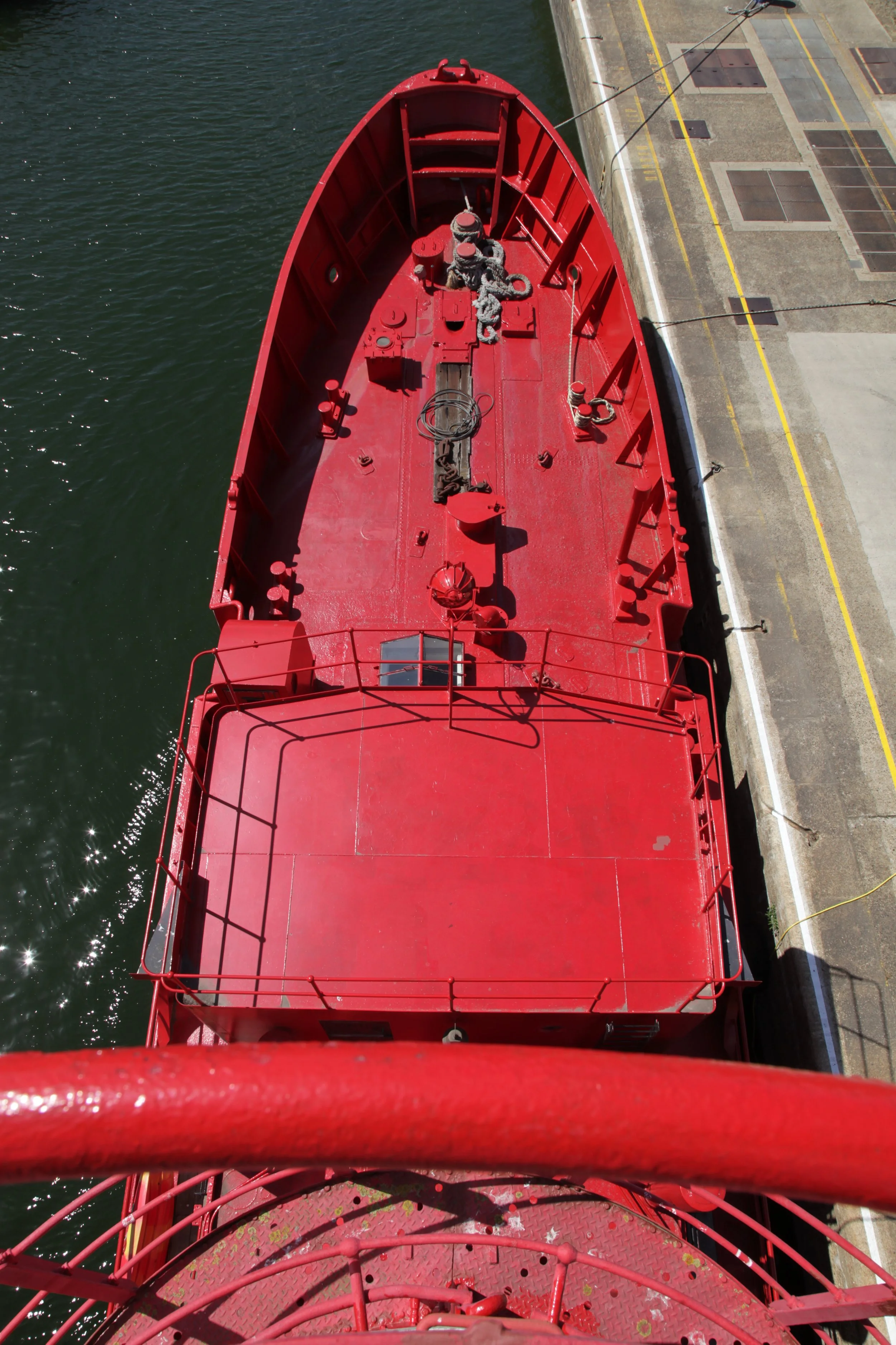 Top view of a red fireboat docked next to a concrete pier, showing the deck with equipment and ropes.