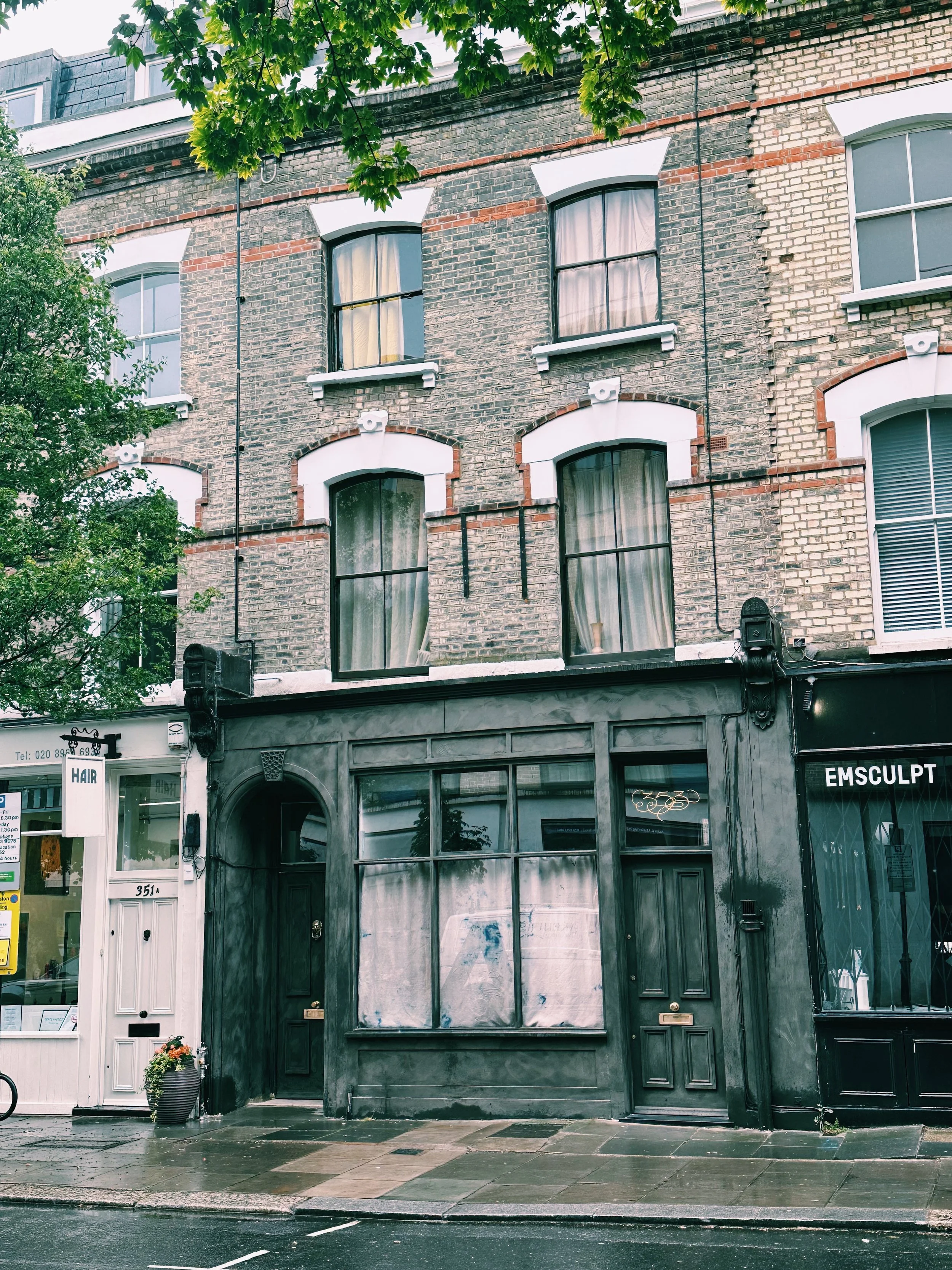 Street view of a multi-story brick building with a salon and a beauty clinic on the ground floor, with trees and shops on the sidewalk.