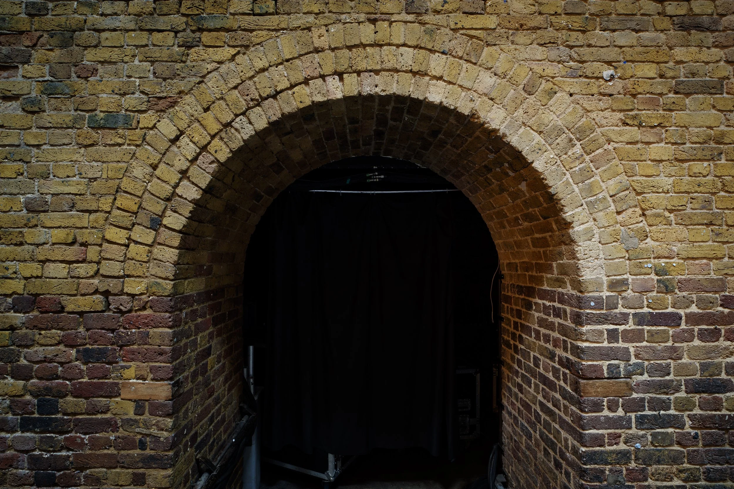 Archway made of yellow and red bricks on a brick wall, leading into a dark space.
