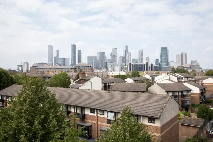 City skyline with tall skyscrapers in the background and residential houses with trees in the foreground.
