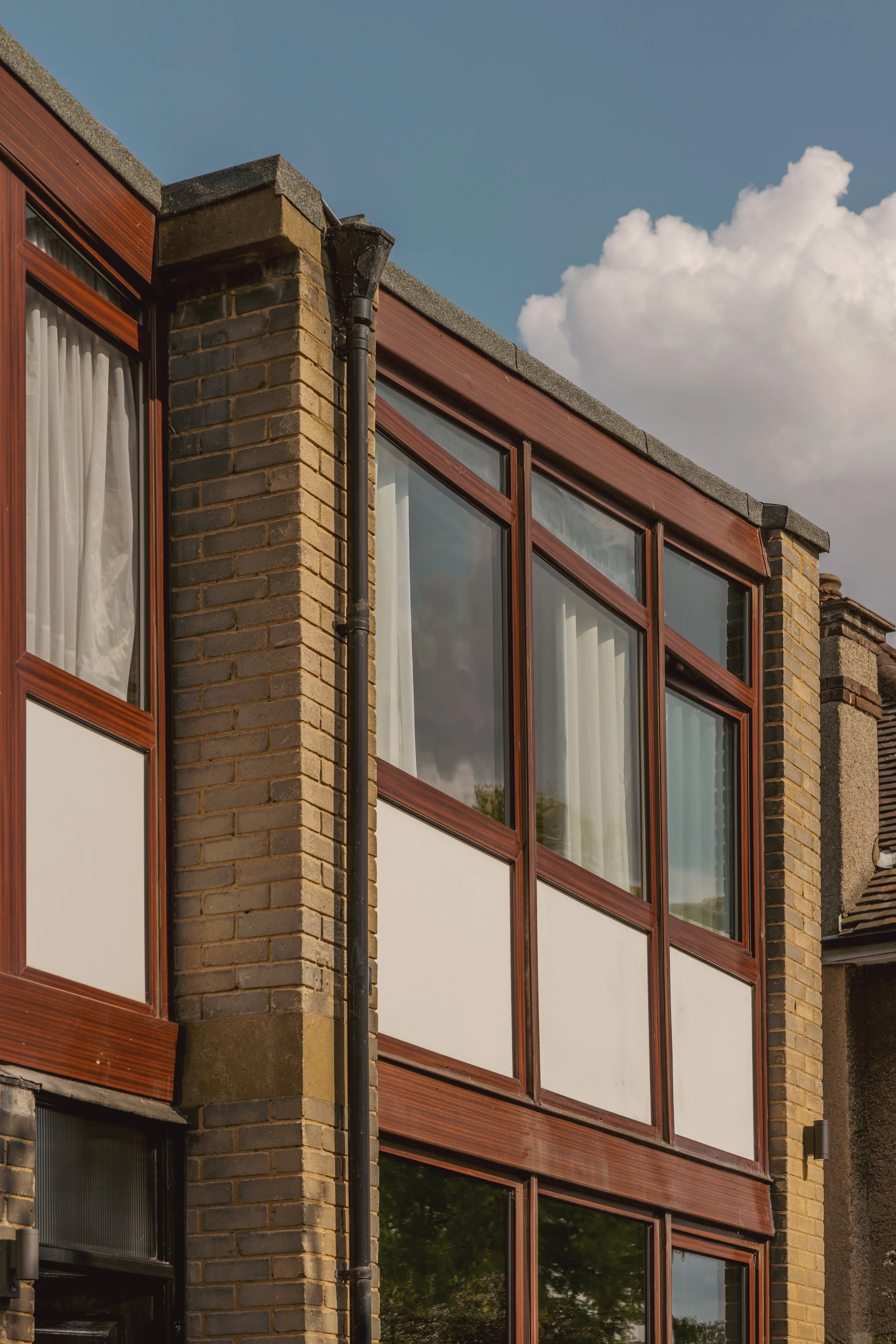 Close-up of a modern apartment building with large glass windows framed in wood, brick and no curtains, under a partly cloudy sky.