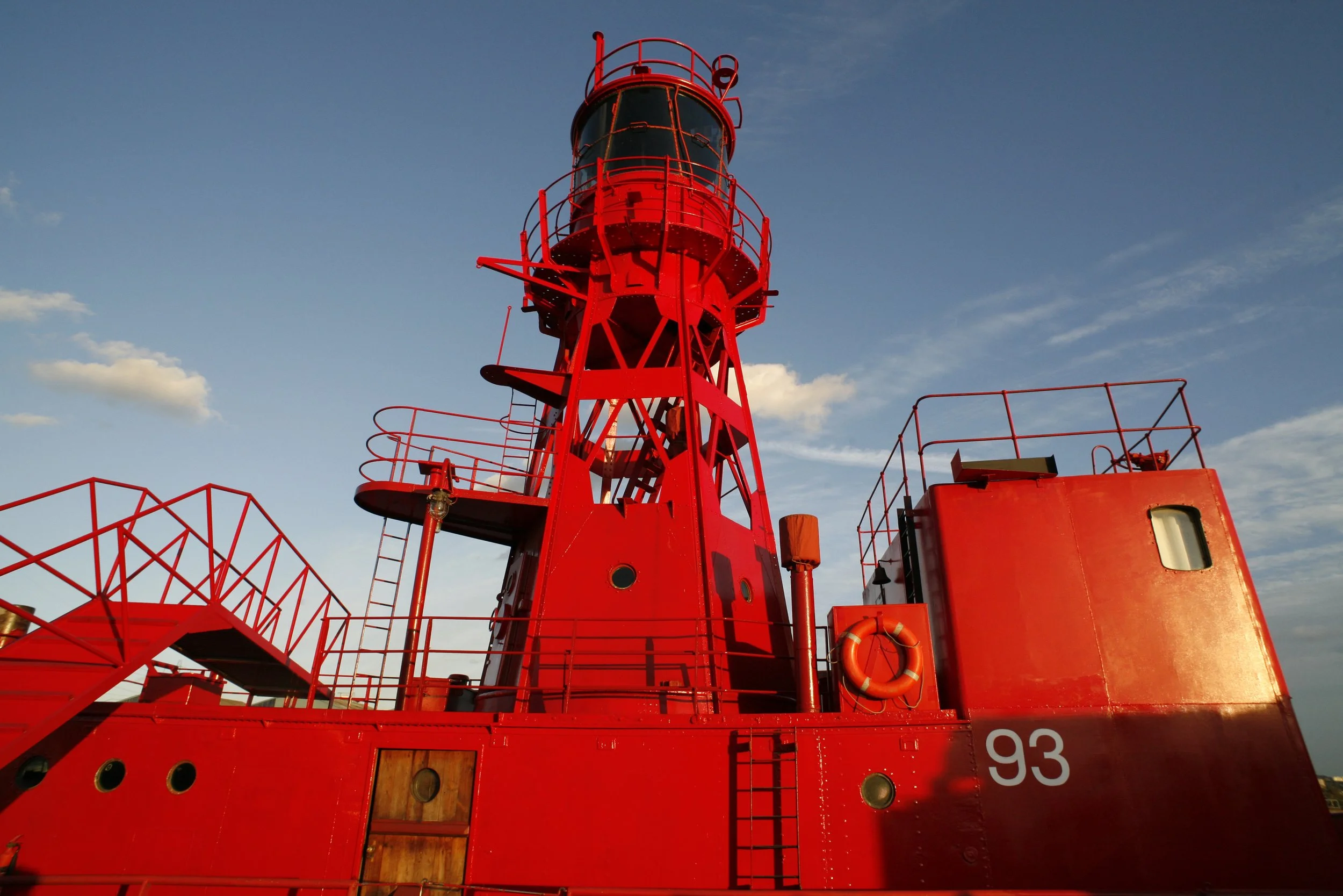 Close-up of a bright red lighthouse on a ship with the number 93, against a blue sky with scattered clouds.