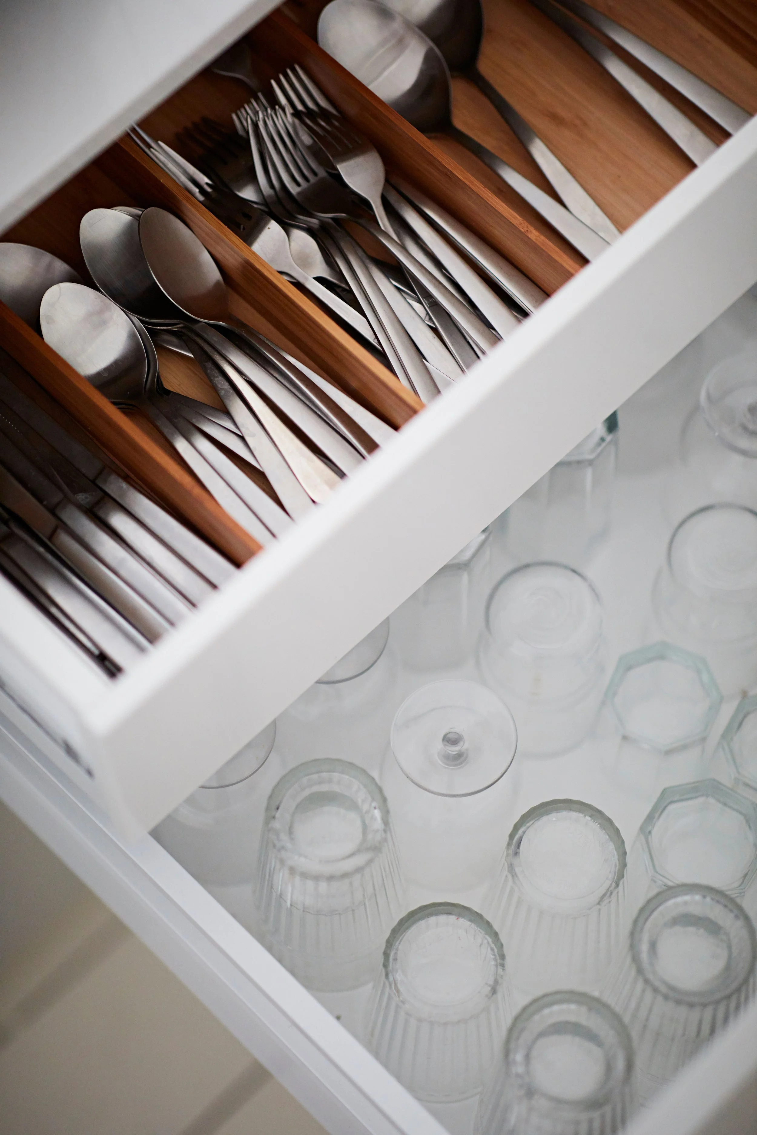 Drawer with metal spoons and forks in a wooden organizer and upside-down glassware.