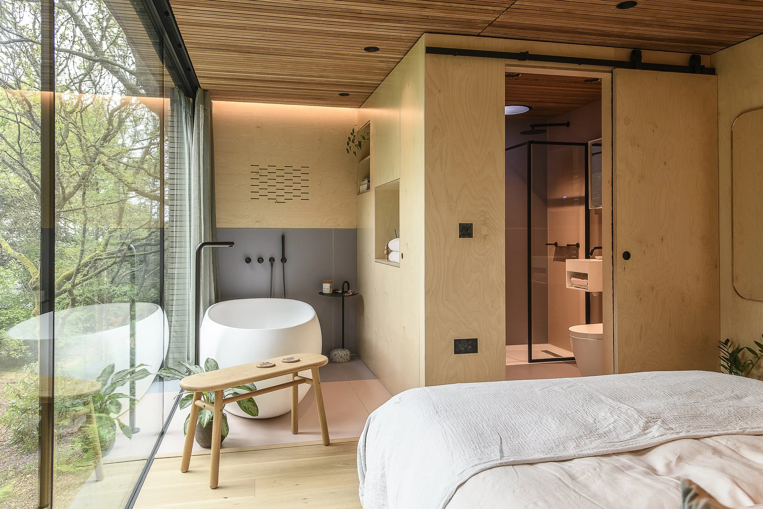 A cozy bedroom with a large bed, a bathtub near a window, and a small adjoining bathroom with a shower and toilet.