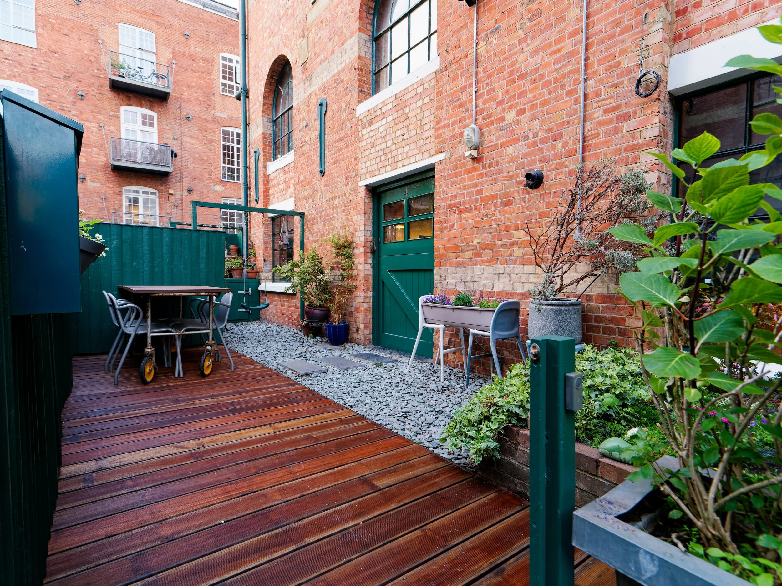 Small urban patio with red brick walls, wooden deck, outdoor furniture, and potted plants.