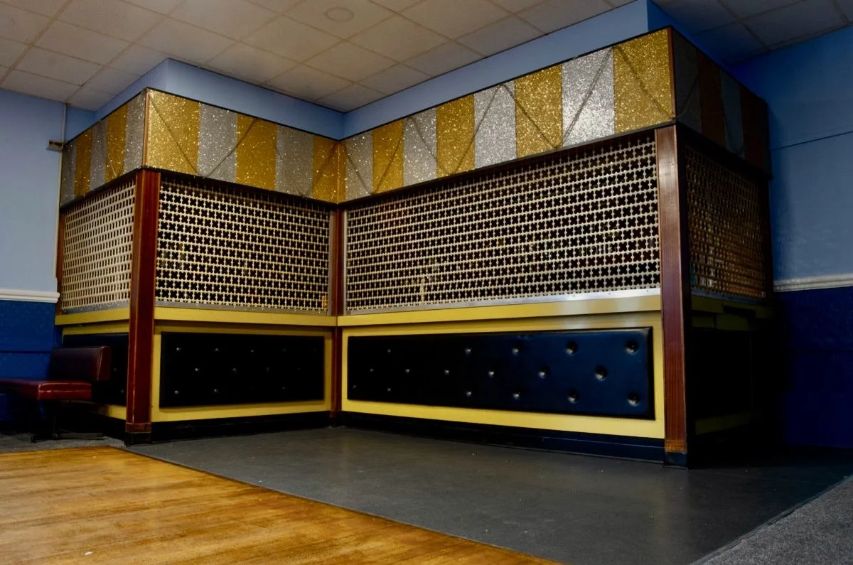 Corner of a room with decorative wooden panels, gold and silver glittery triangles, and black and yellow padded upholstery.