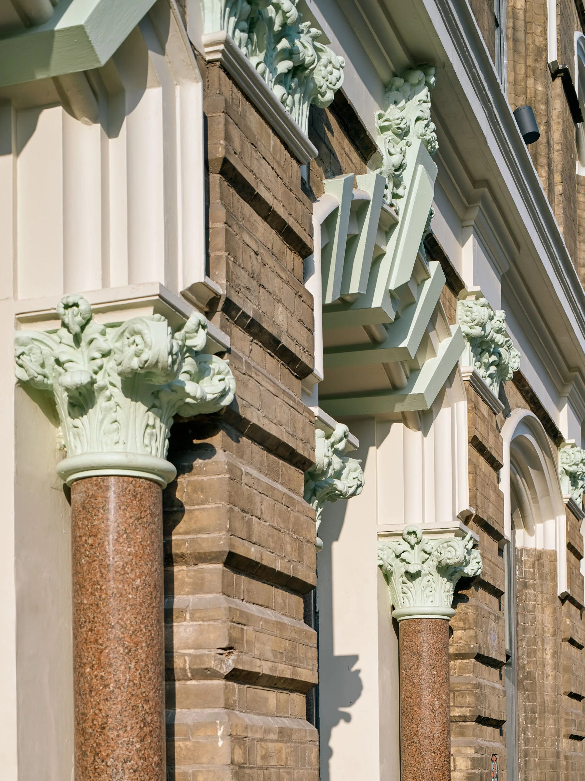 Close-up of building facade with brick and stone columns, ornate corbels, and decorative window frames.