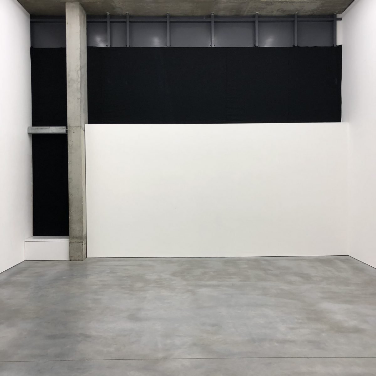 Empty gallery with white and black walls, concrete pillar, and gray floor.