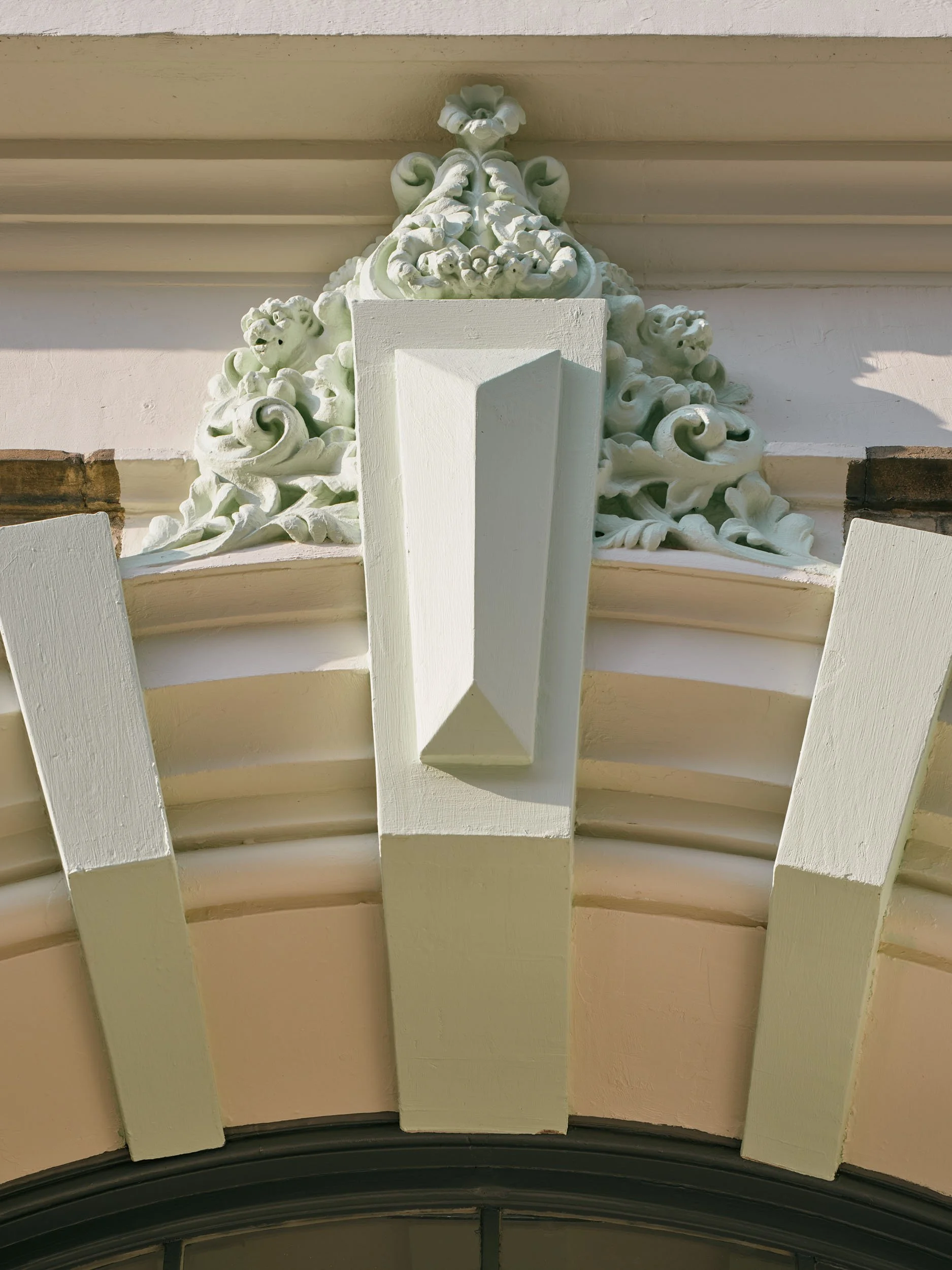 Close-up of decorative white architectural ornamentation above a window, featuring intricate scrollwork and floral designs.