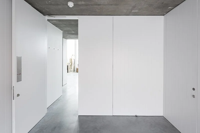 Modern interior with white sliding doors and concrete ceiling, hallway with natural light.