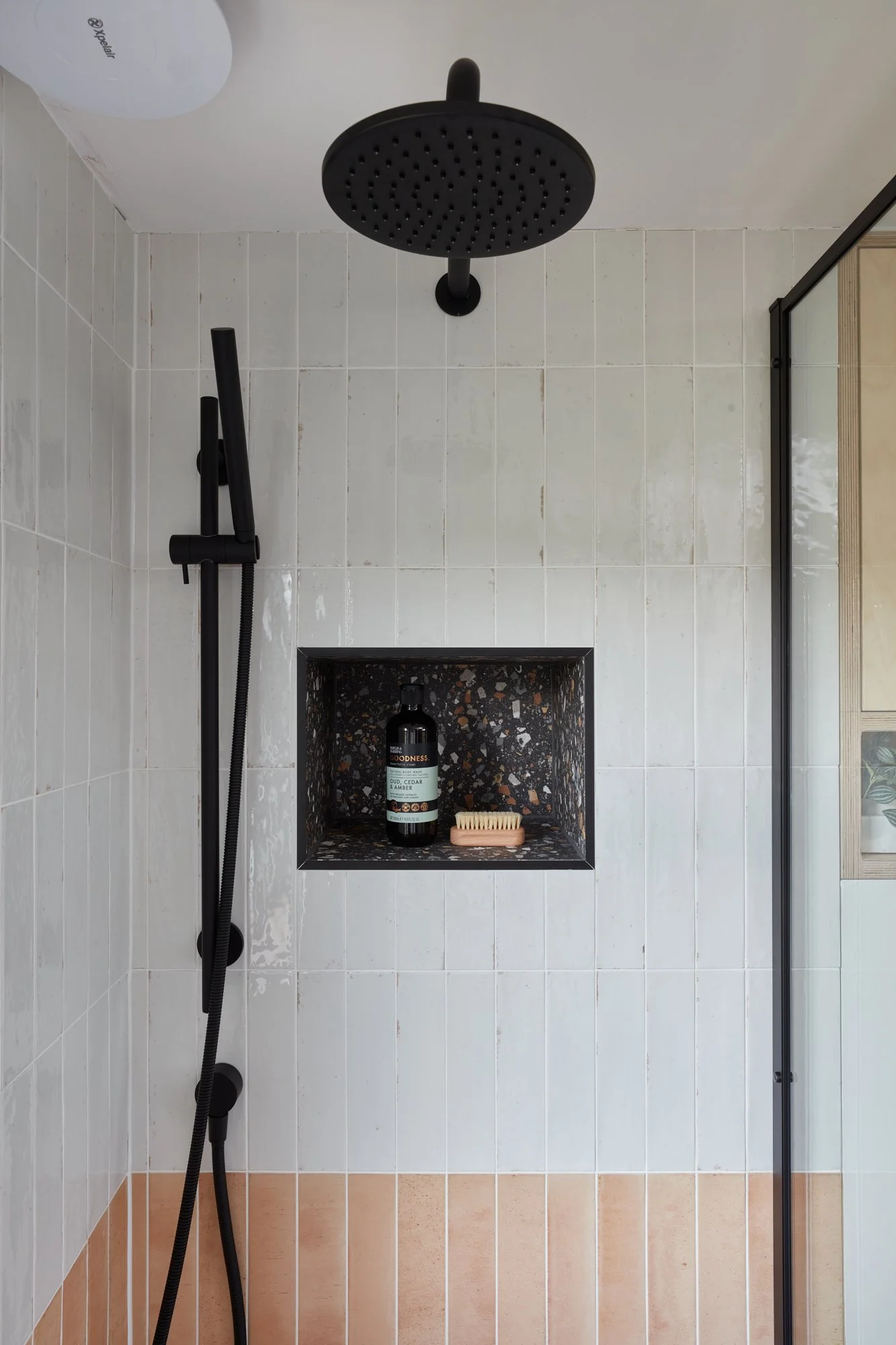Shower with black rainfall showerhead, handheld shower, and built-in niche with soap and shampoo bottles.