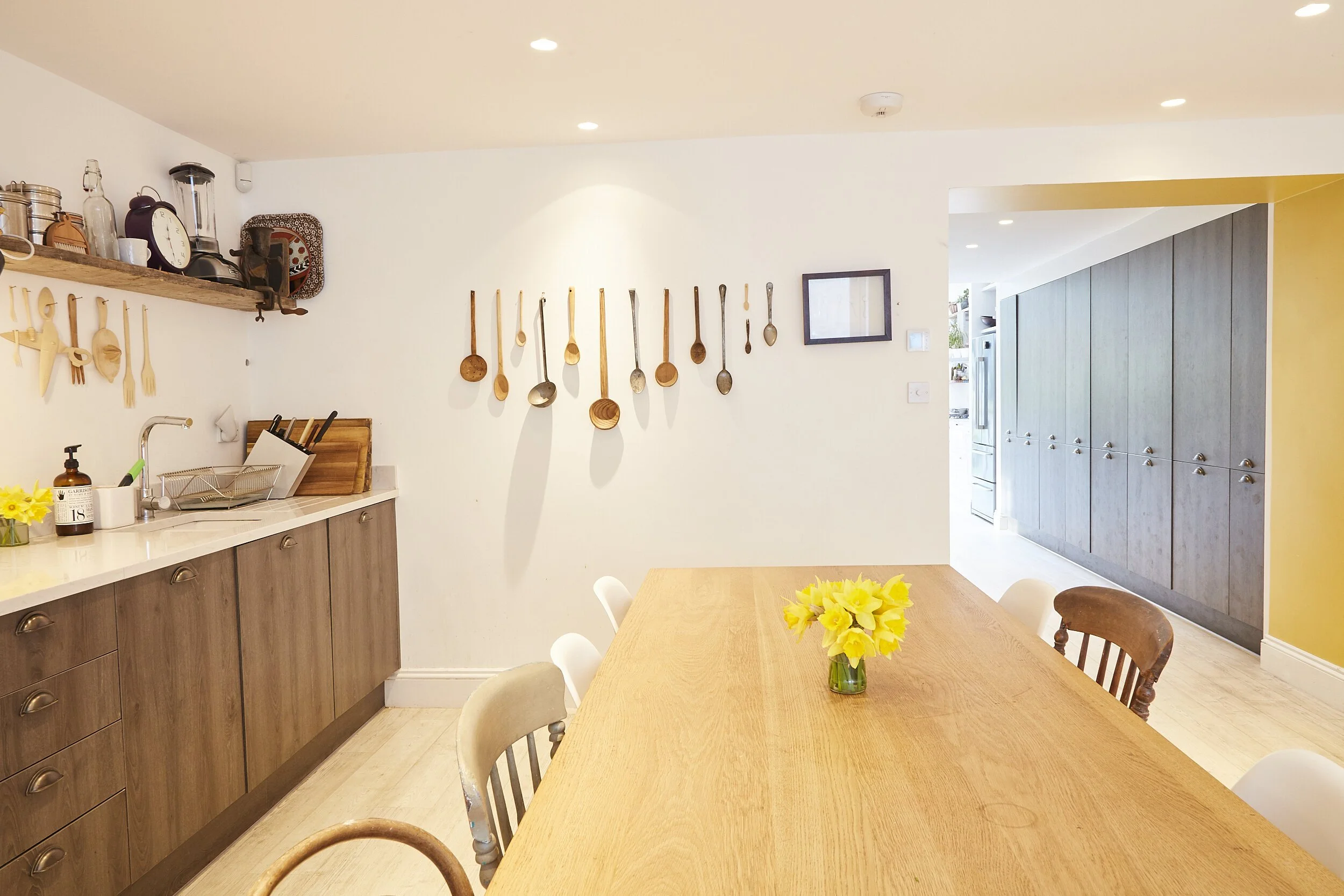 A bright kitchen and dining area with wooden countertops, a table with yellow flowers, and decorative wooden spoons hanging on the wall.