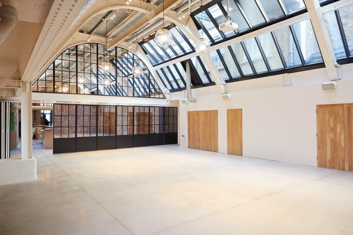 Empty industrial-style room with high glass ceiling and wooden doors.
