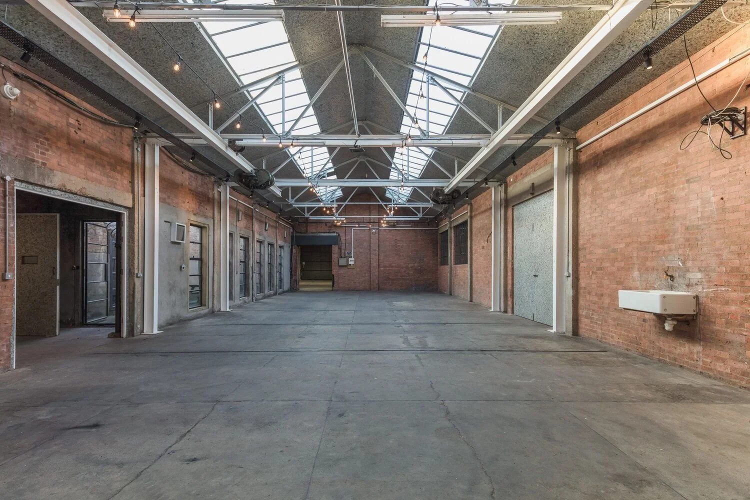 An empty industrial-style interior with brick walls, large skylights, and exposed ceiling beams.