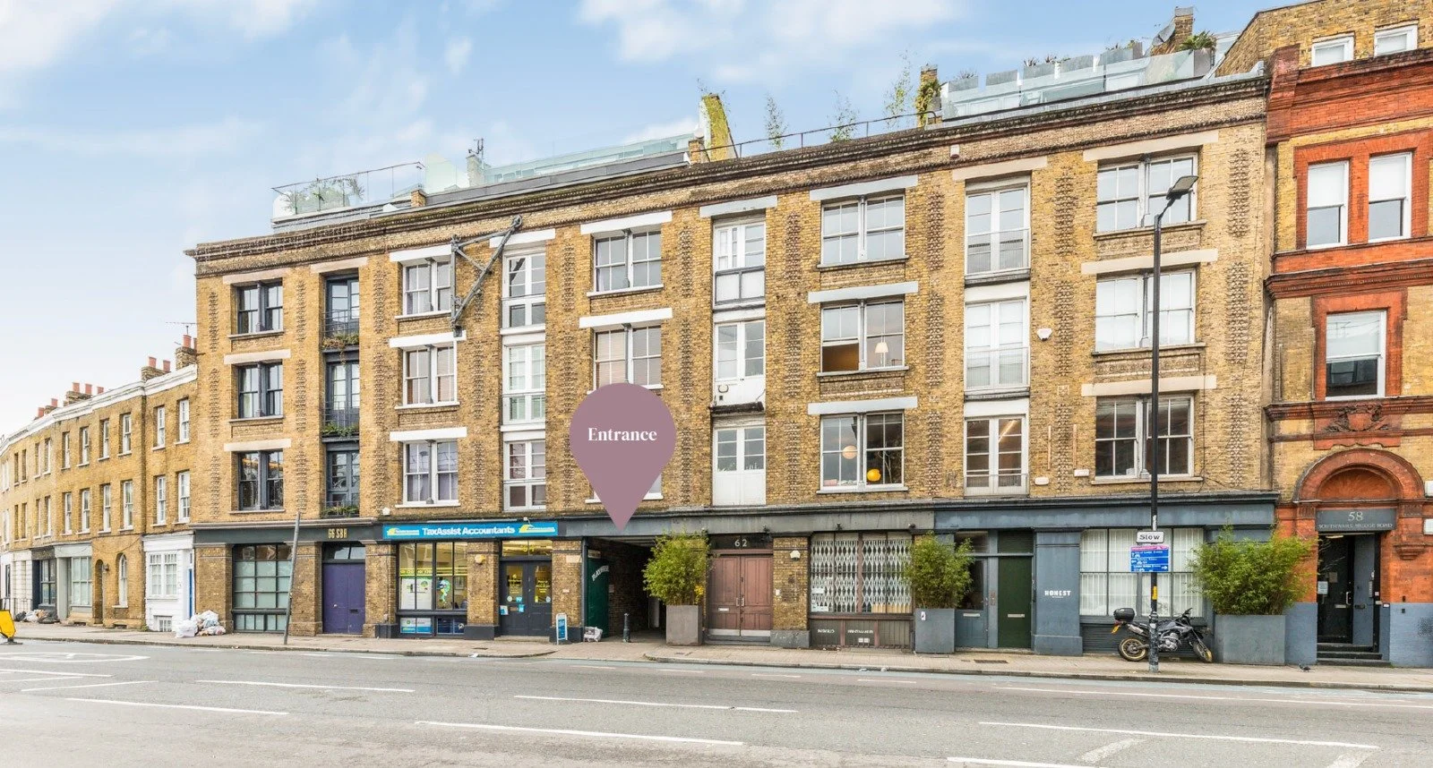 Urban street view of a multi-story brick building with commercial spaces on the ground floor and residential apartments above, including a sign for TaxAssist Accountants and an entrance marked with a purple label.