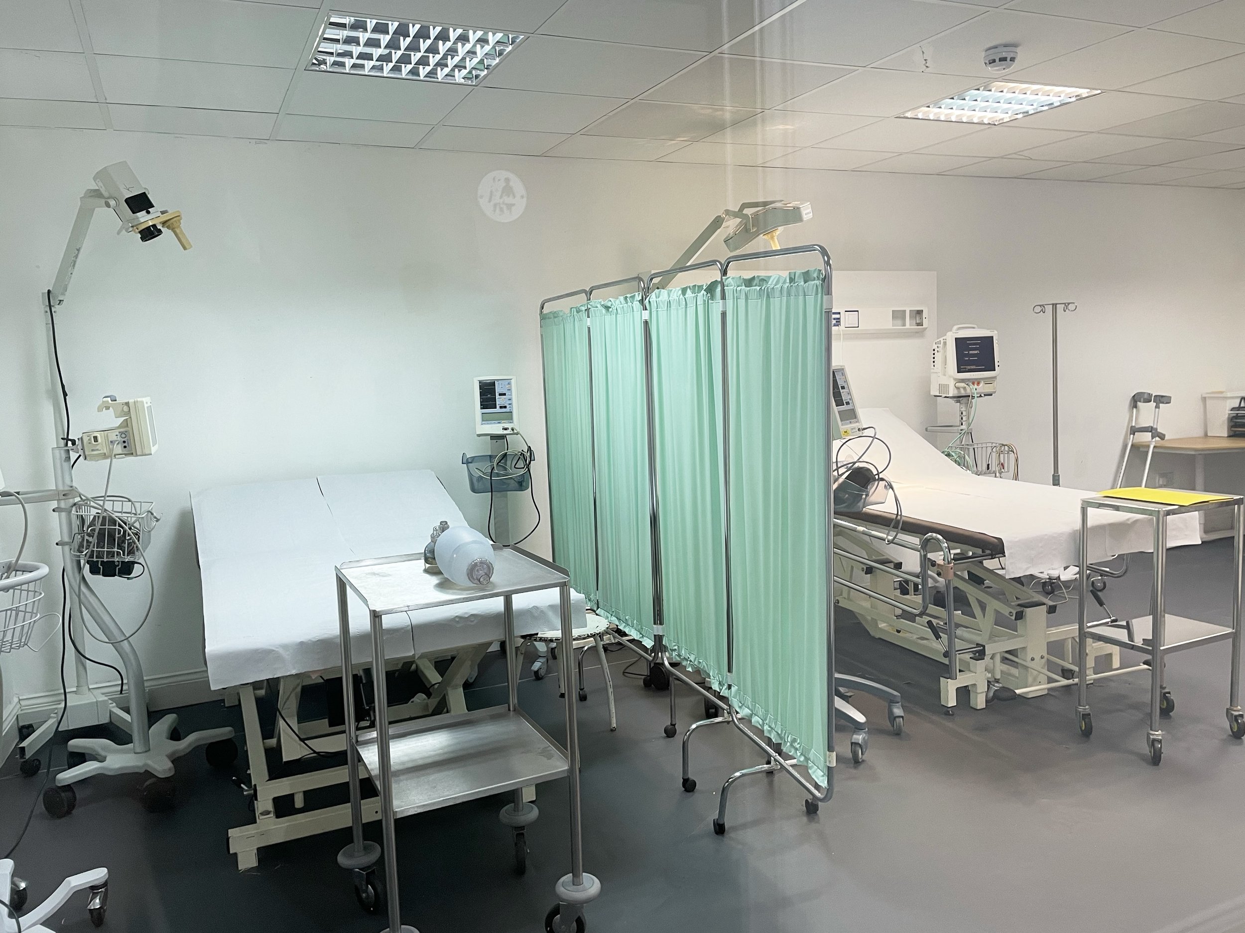 Hospital room with two beds, medical equipment, monitors, and a privacy curtain.