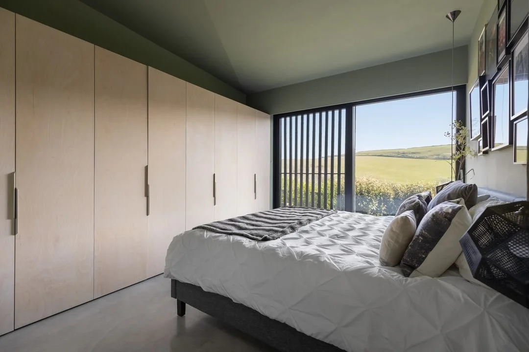 Modern bedroom featuring a large bed with pillows and a blanket, a wall of beige closets, and sliding glass doors overlooking a grassy landscape.
