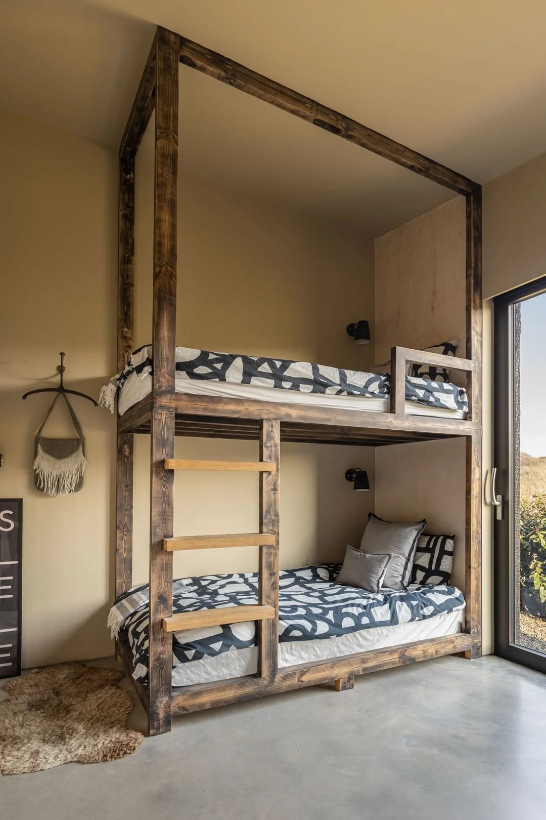 Loft-style bedroom with a wooden bunk bed, black and white patterned bedding, and gray pillows, next to a large sliding glass door.