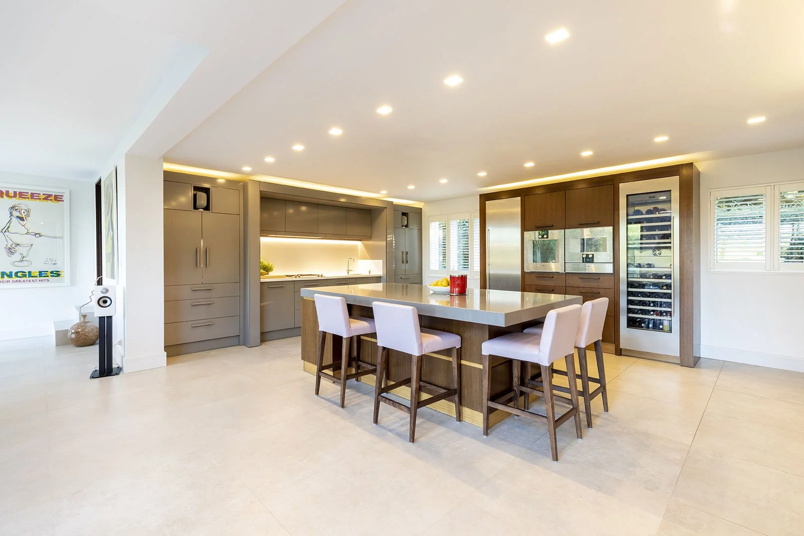 Modern open-concept kitchen with gray cabinets, white countertops, kitchen island with seating, wine refrigerator, and large windows