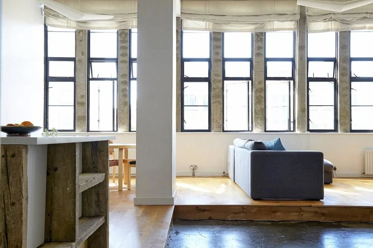 Living room with large windows, a gray sofa, and wooden flooring