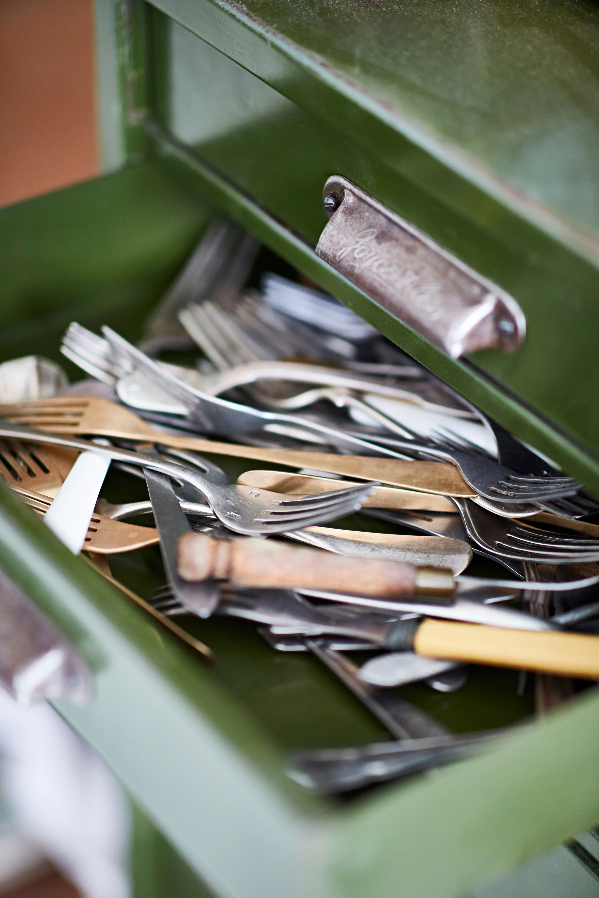 A drawer filled with used forks and knives in a green metal box.
