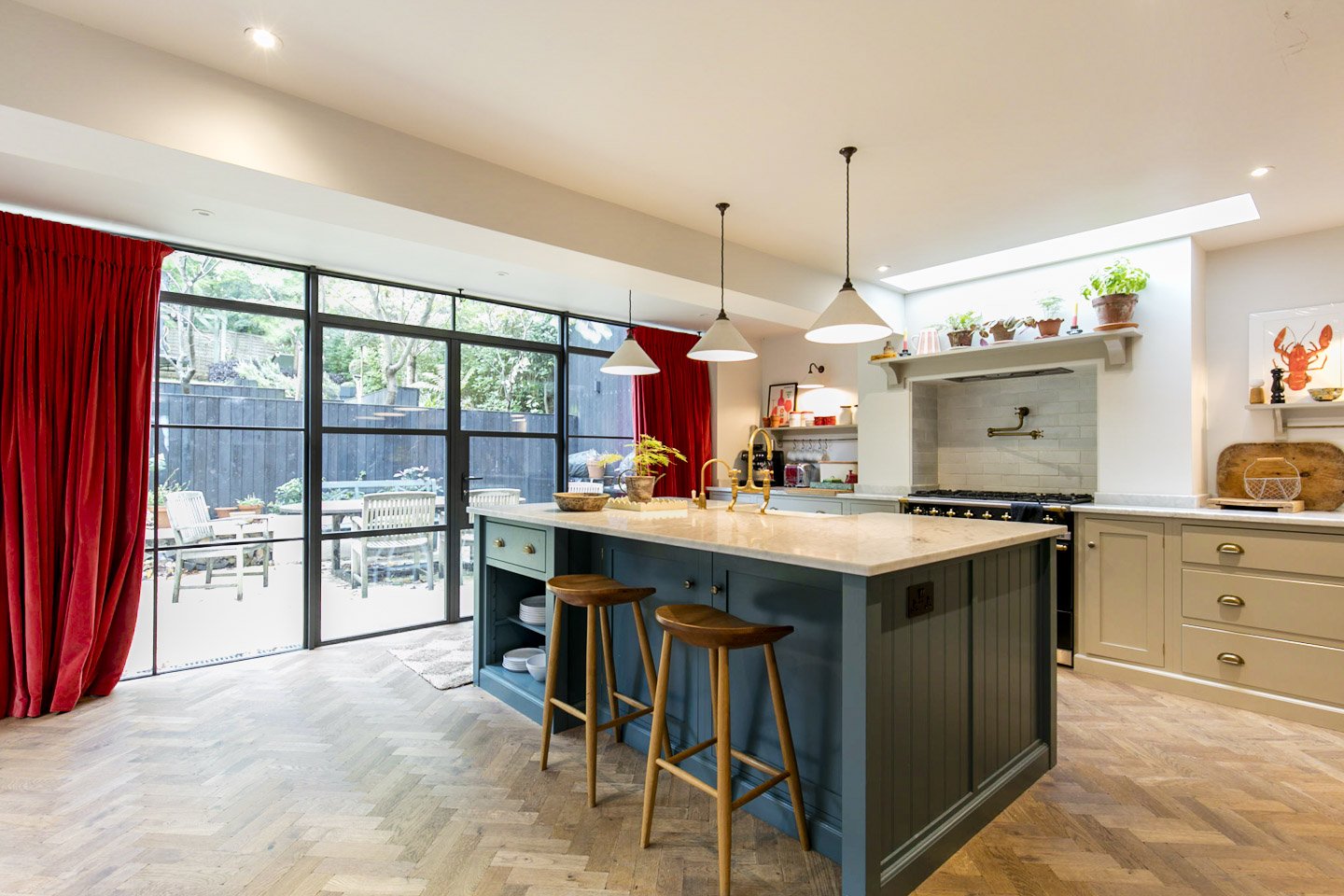 Modern kitchen with blue island, white countertops, gold fixtures, and open view to outdoor patio with table and chairs.