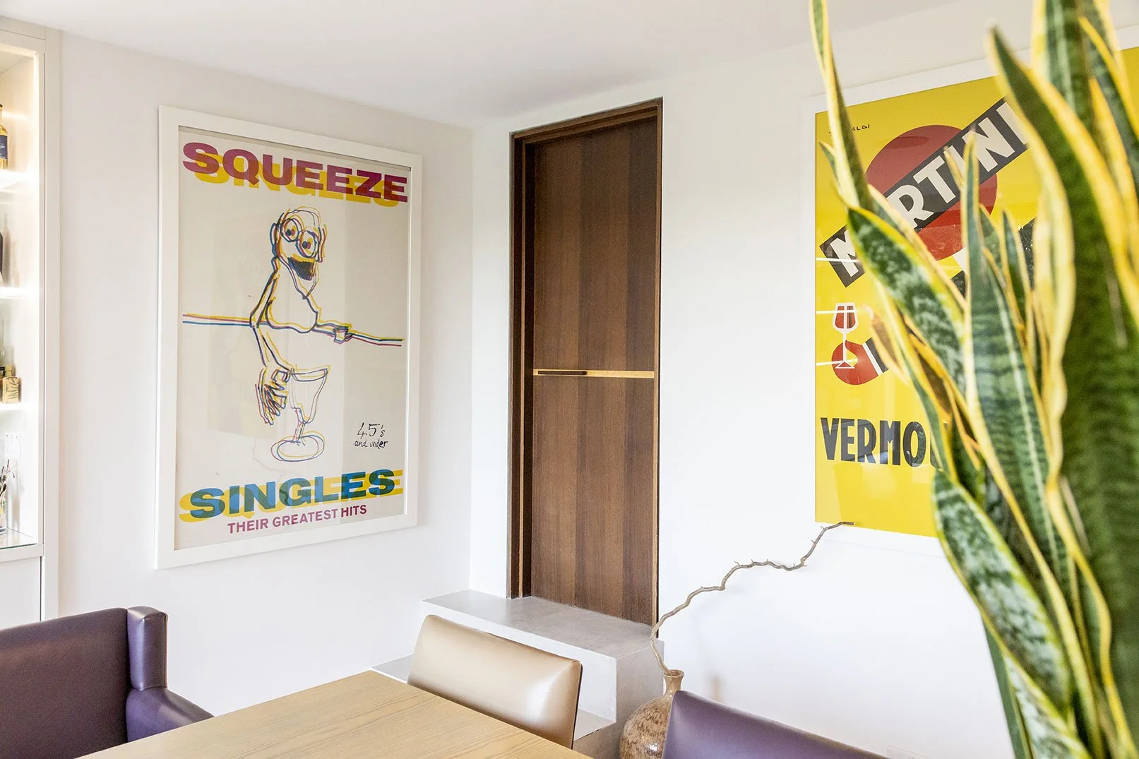 A room with white walls decorated with colorful posters. One poster reads 'Squeeze Singers Their Greatest Hits' with a line drawing of a smiling cartoon figure holding a microphone. Another poster has a yellow background with black and red text and g