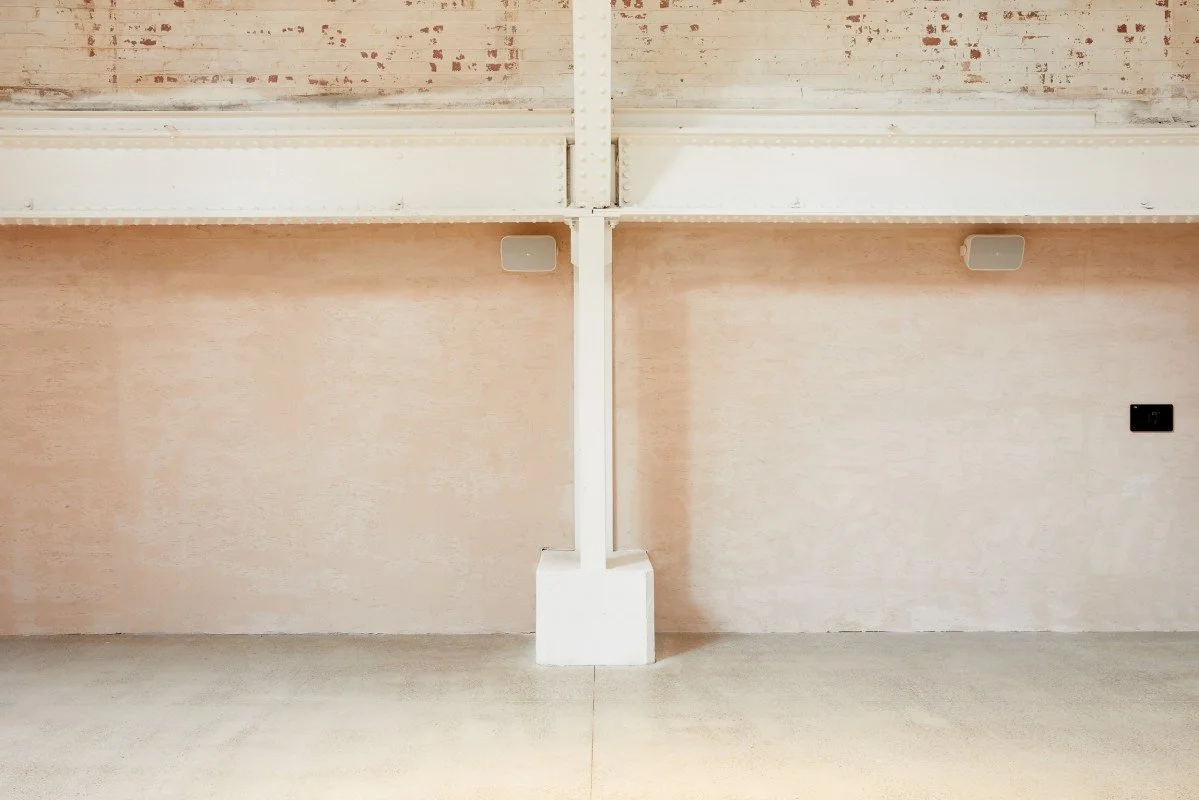 Empty room with a beige wall, exposed ceiling beams, and a white support column in the center.