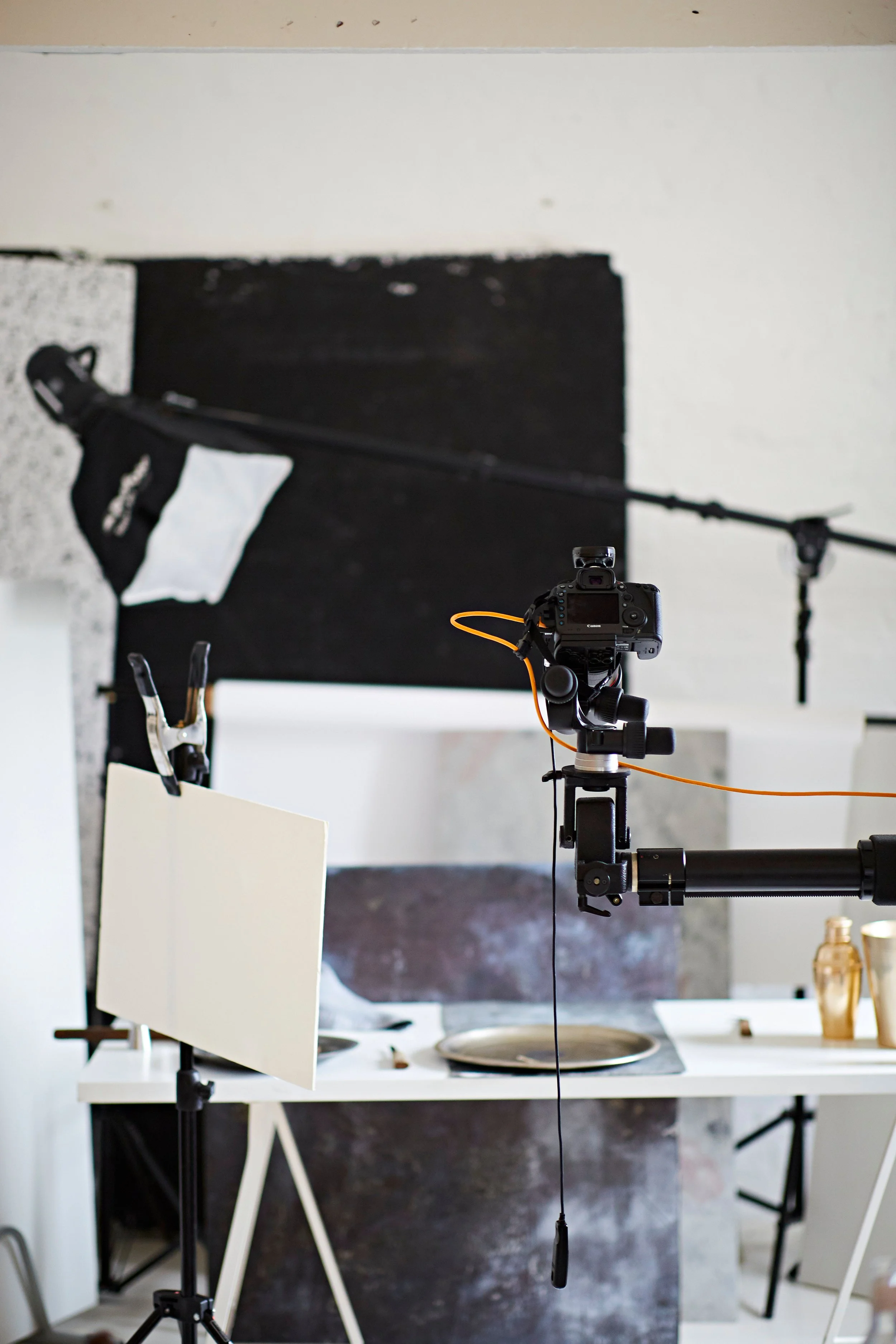Indoor photography/setup with camera on tripod, photography lighting equipment, and a black and white backdrop in the background.