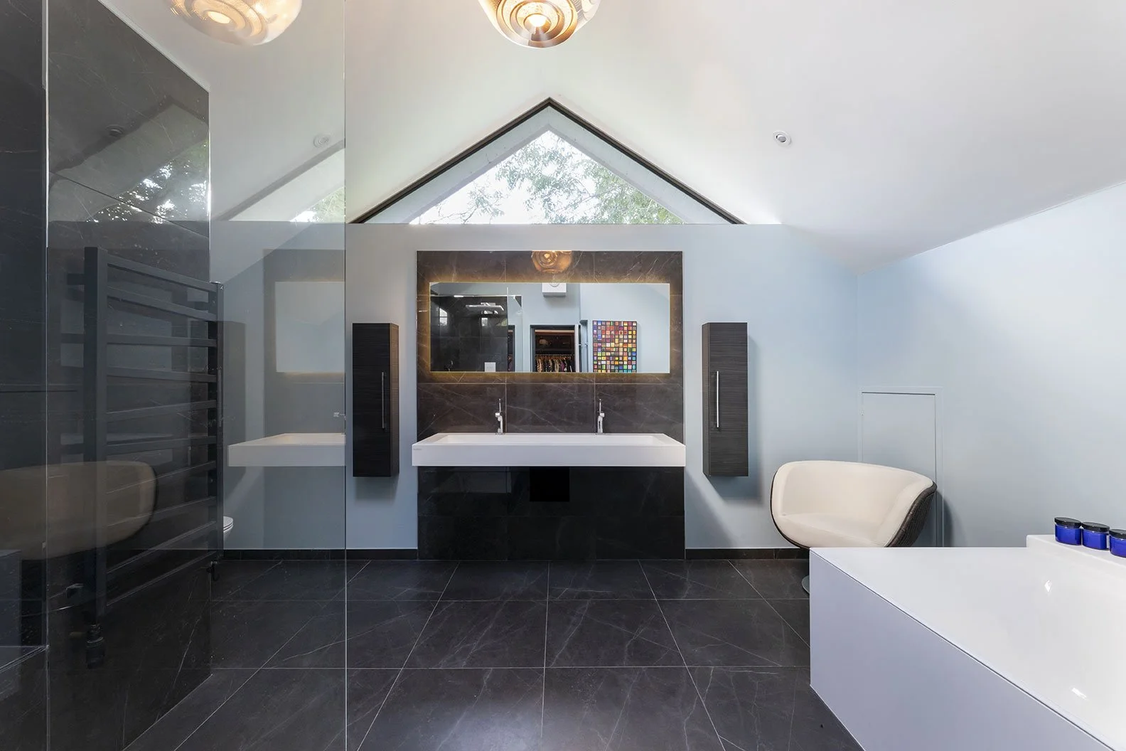 Modern bathroom with a large window, double sink vanity with a mirror, black and white color scheme, white chair, and blue candles on a white tub or counter.