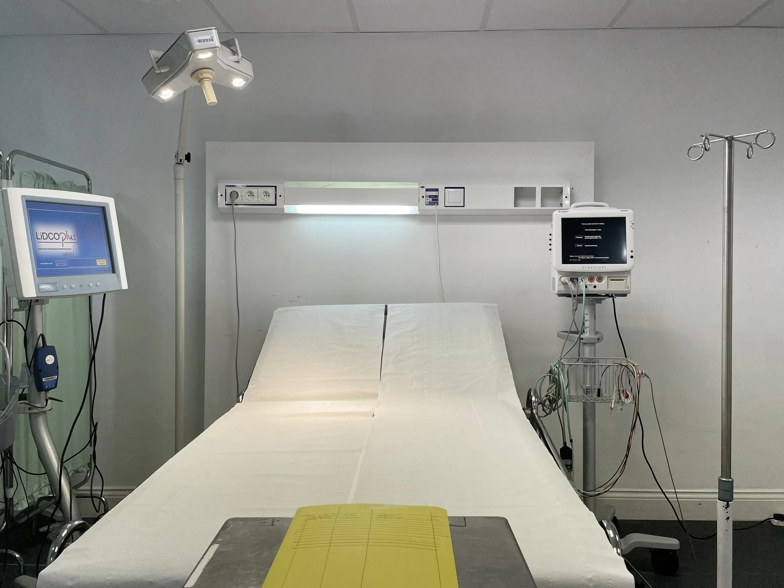 Empty hospital bed in a patient room with medical monitors and equipment around it.
