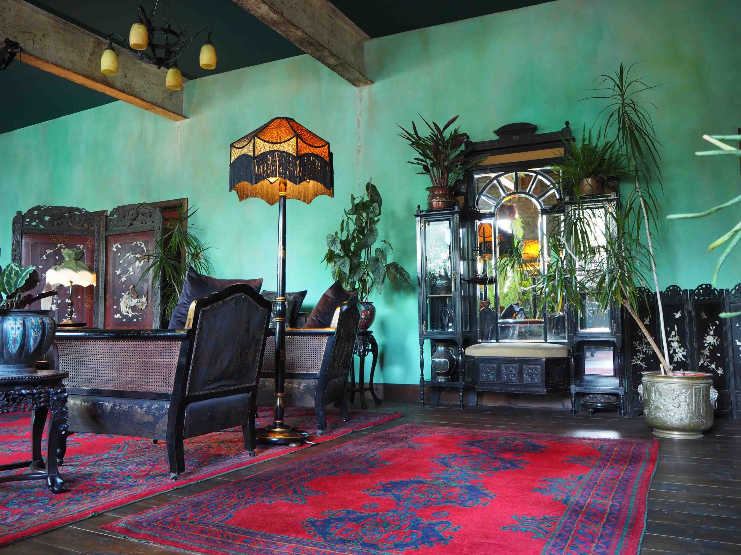 Living room with green wall, vintage black furniture, red patterned rug, and tall potted plants.