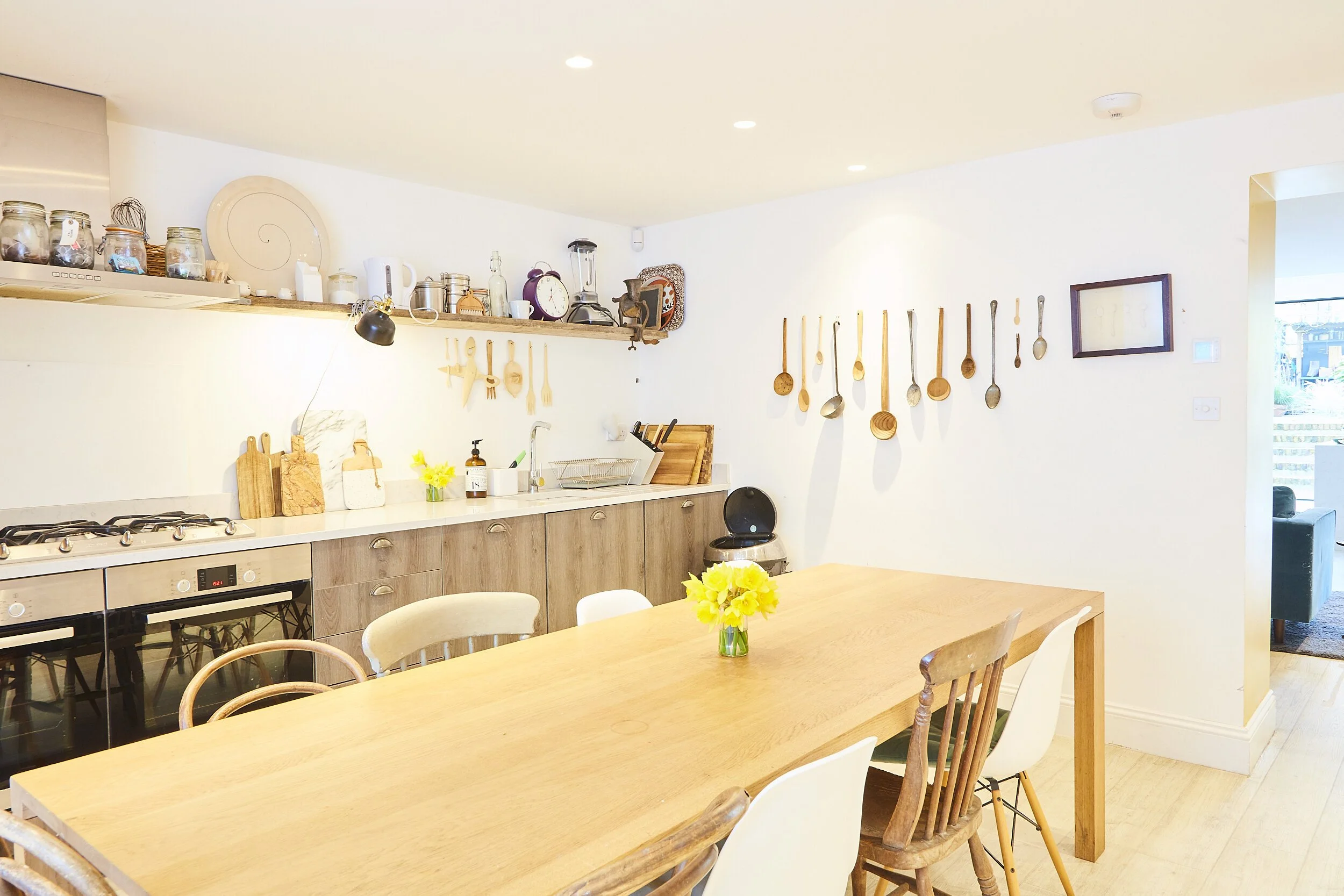 Bright kitchen with wooden dining table, yellow flowers, and kitchen utensils on the wall.