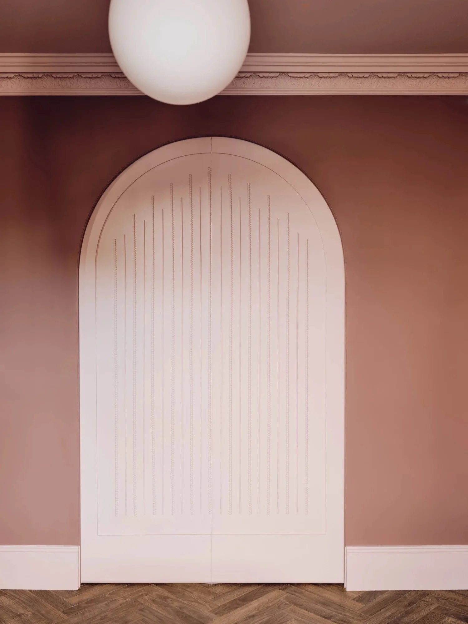 A white arched door with decorative lines on a peach wall, with a white ceiling and a large round white ceiling light above.