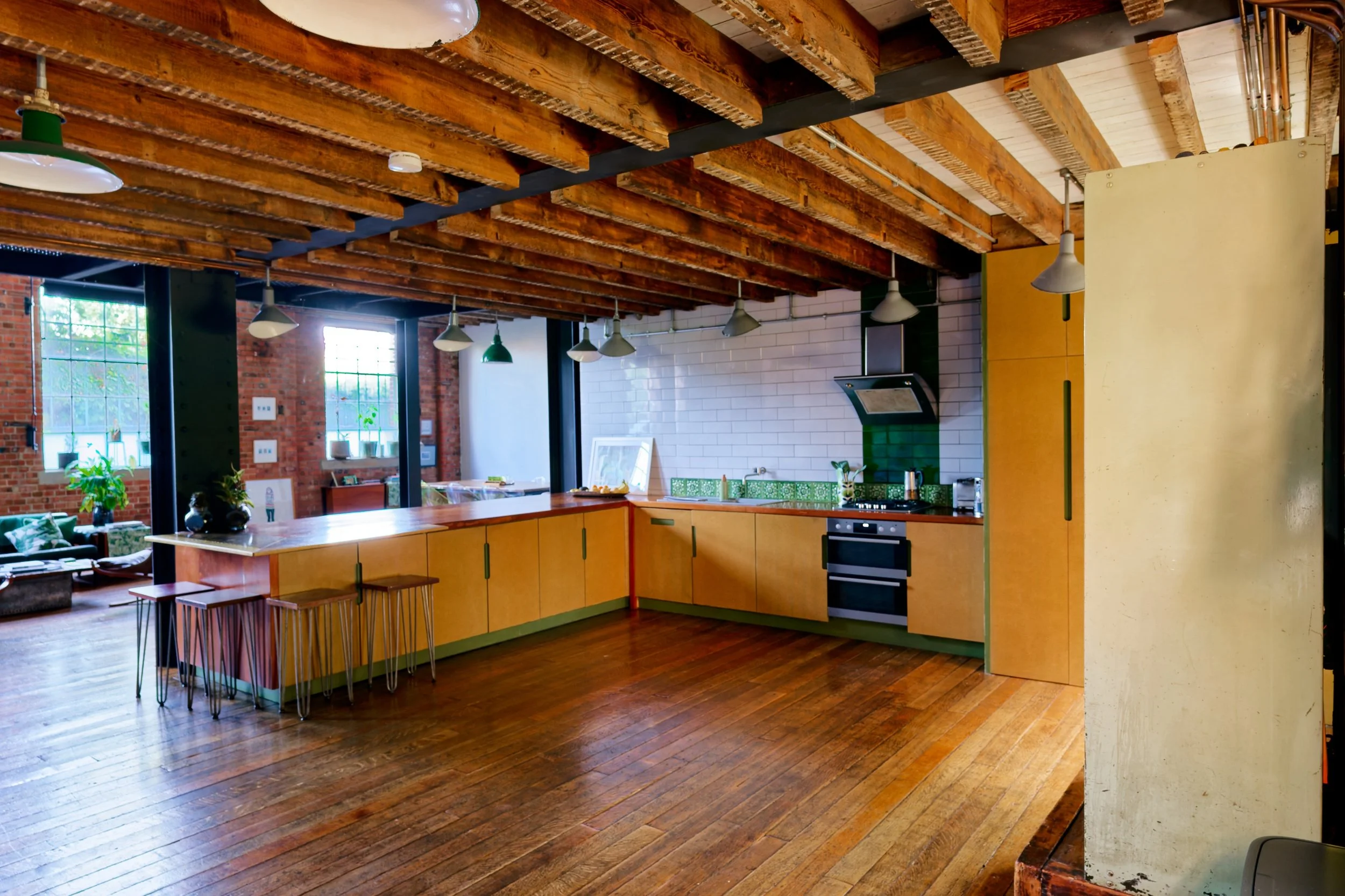 Open kitchen with wooden beams ceiling, yellow cabinets, green and white tiled backsplash, windows with city view, and hardwood flooring.
