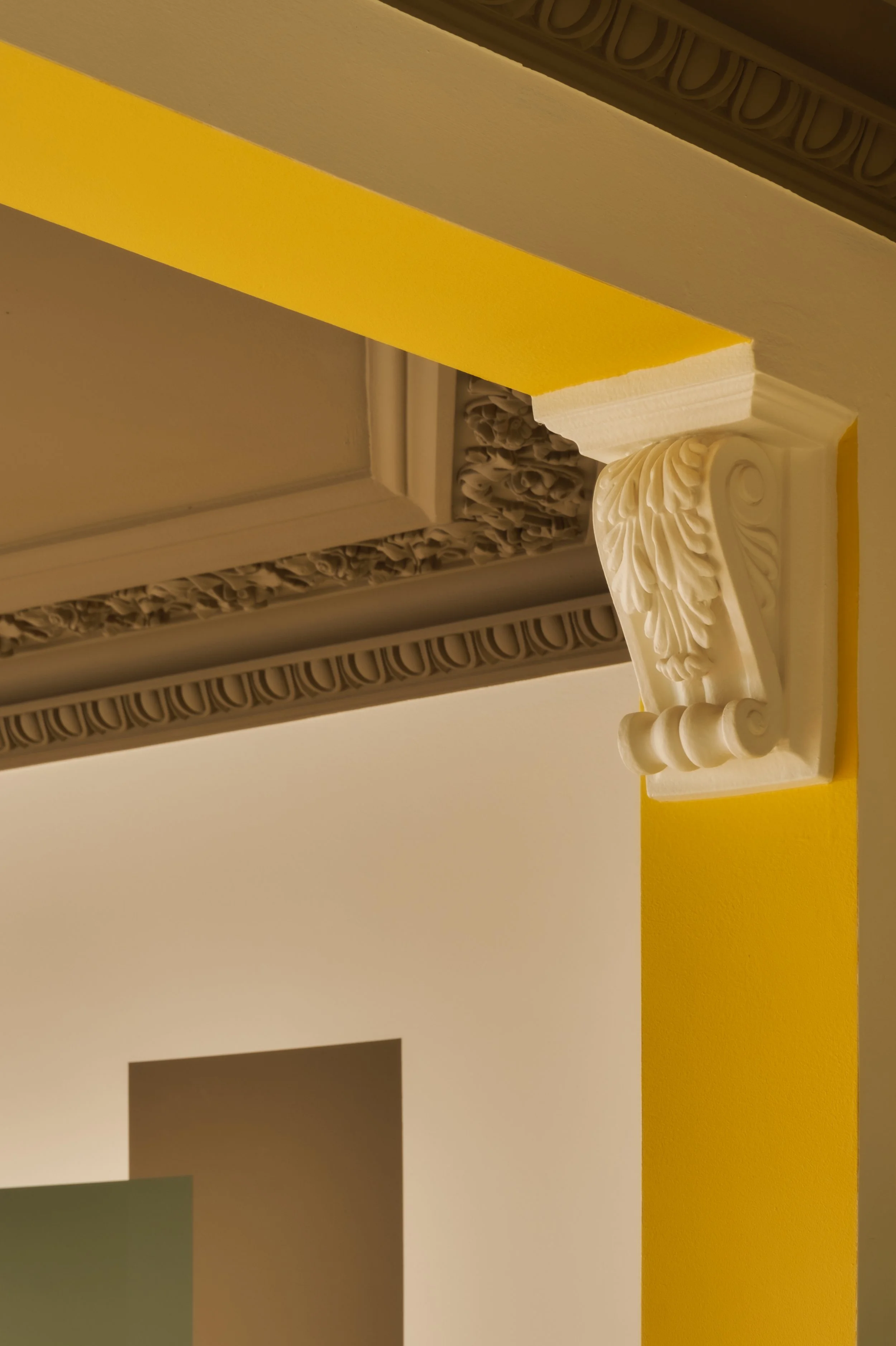 Close-up of ornate architectural molding and decorative corbel on a wall with yellow paint.