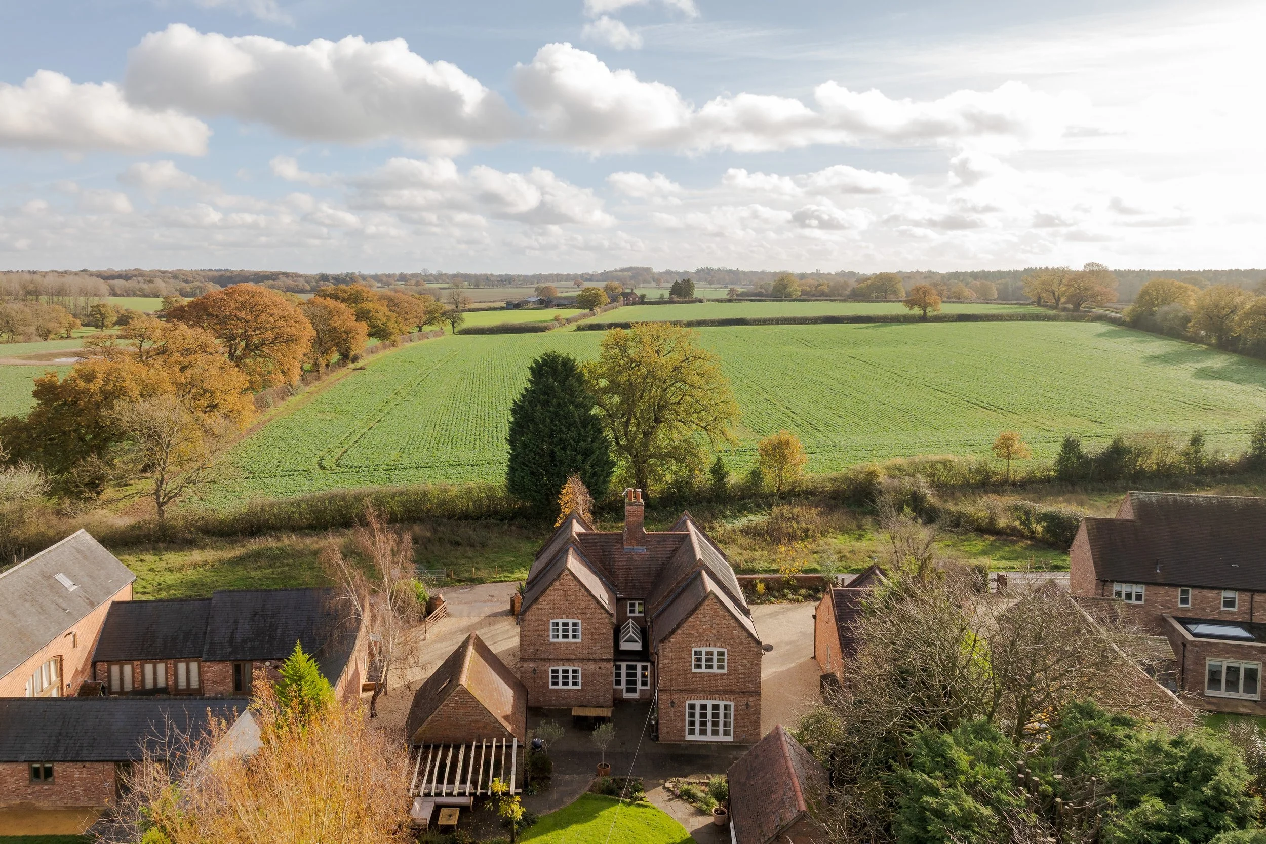 Several houses in a rural area with a green field and trees in the background on a partly cloudy day.