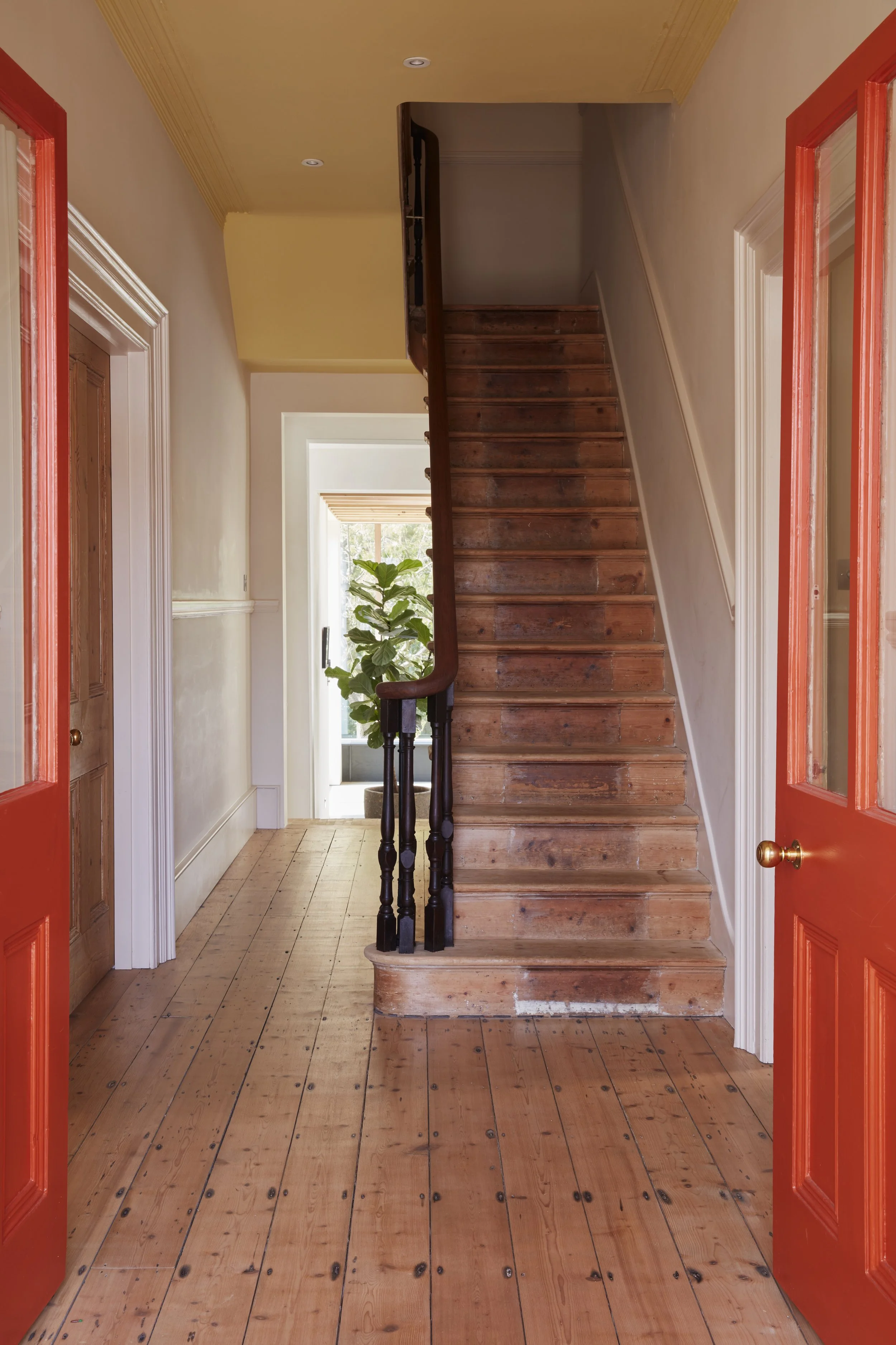 Entryway with wooden floor, a staircase with dark wooden railing, and open red doors leading inside.