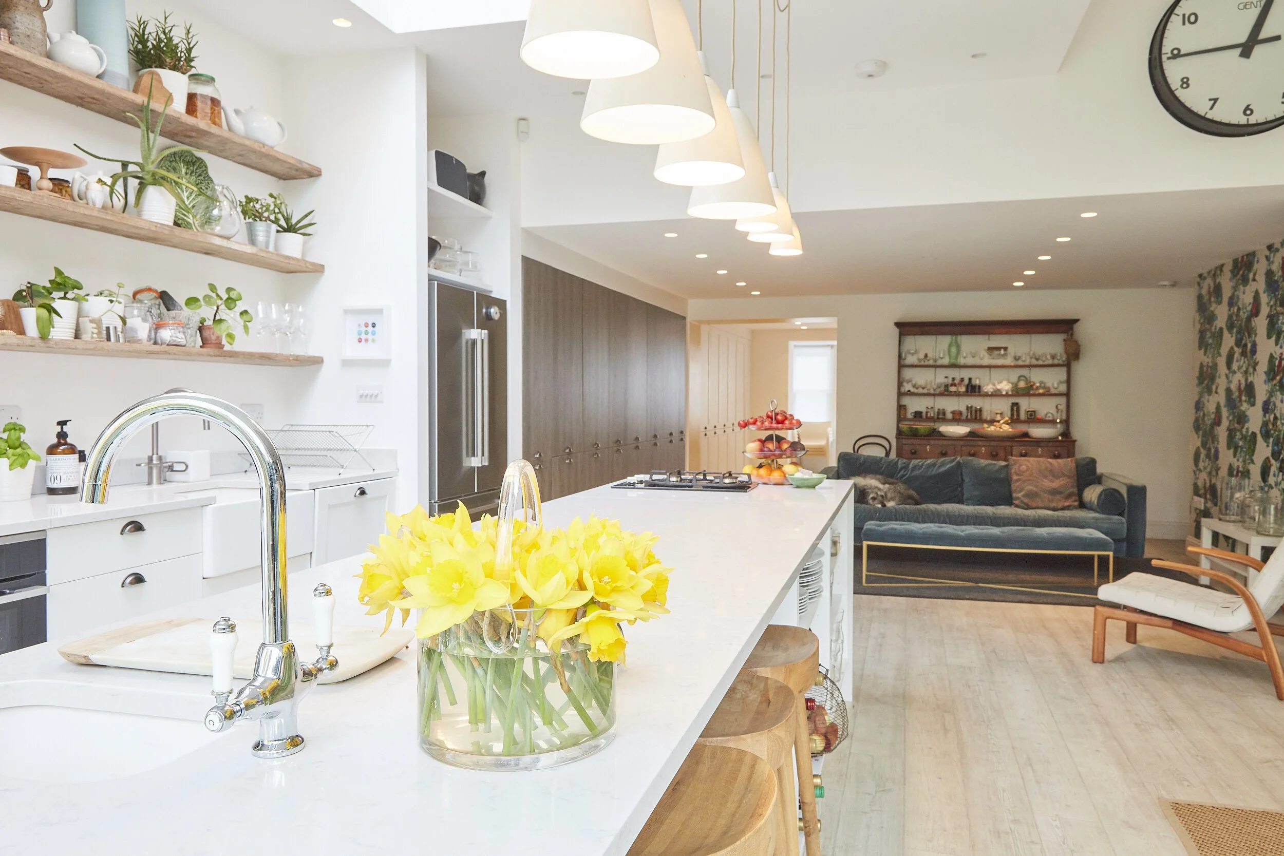 Open-concept kitchen and living room with white island, yellow flowers in a glass vase, and blue sofa in the background.