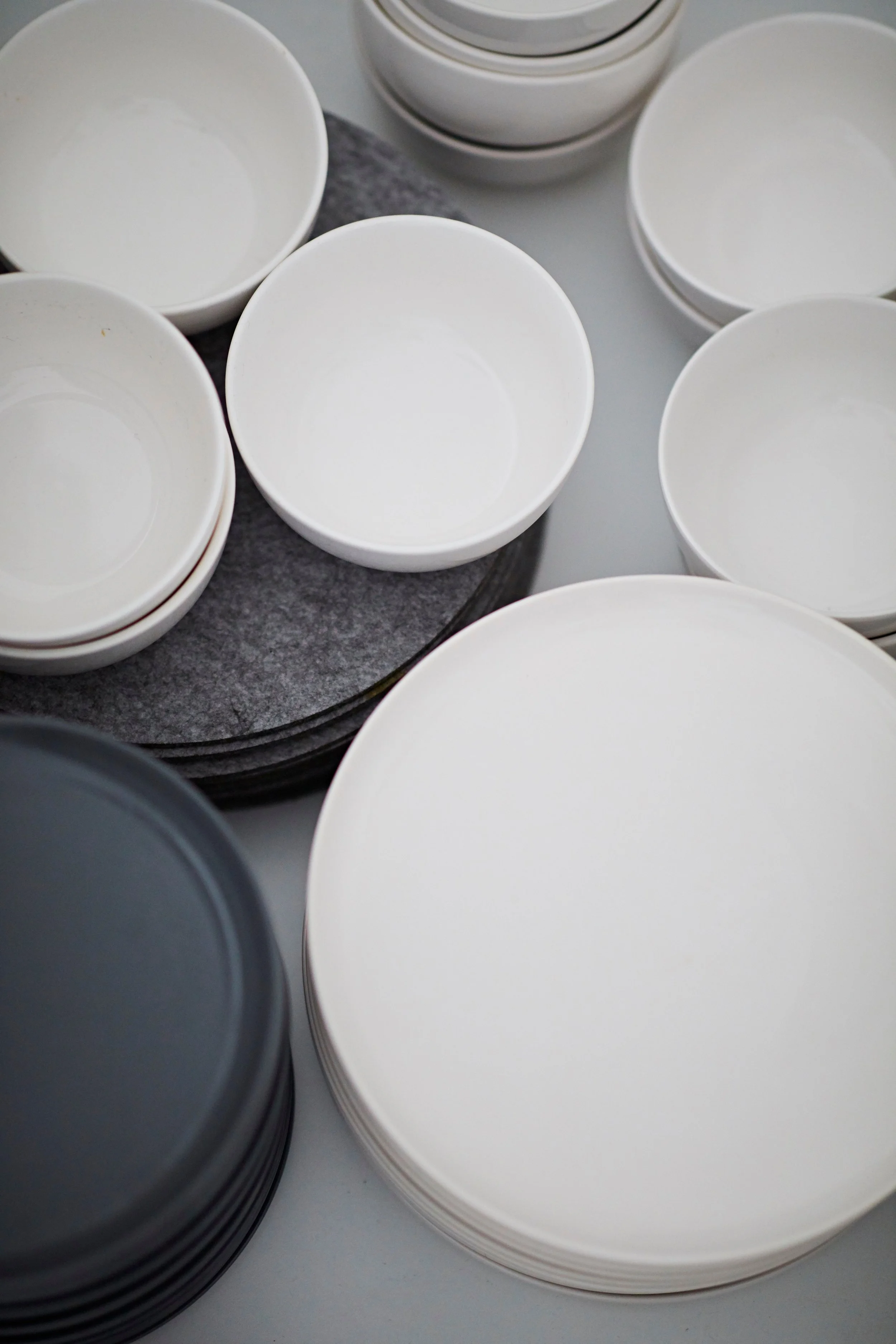 Stacks of white and black ceramic bowls on a gray table, some on a gray felt mat.