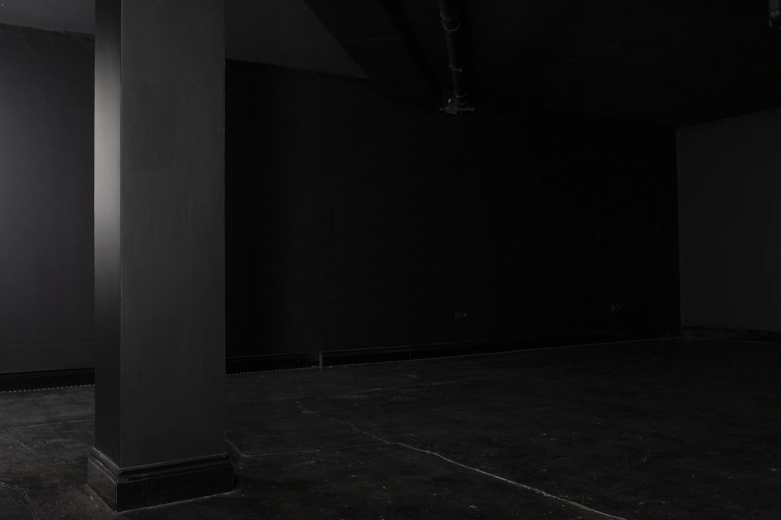 Dark, empty room with black walls, black floor, and a black column in the foreground.
